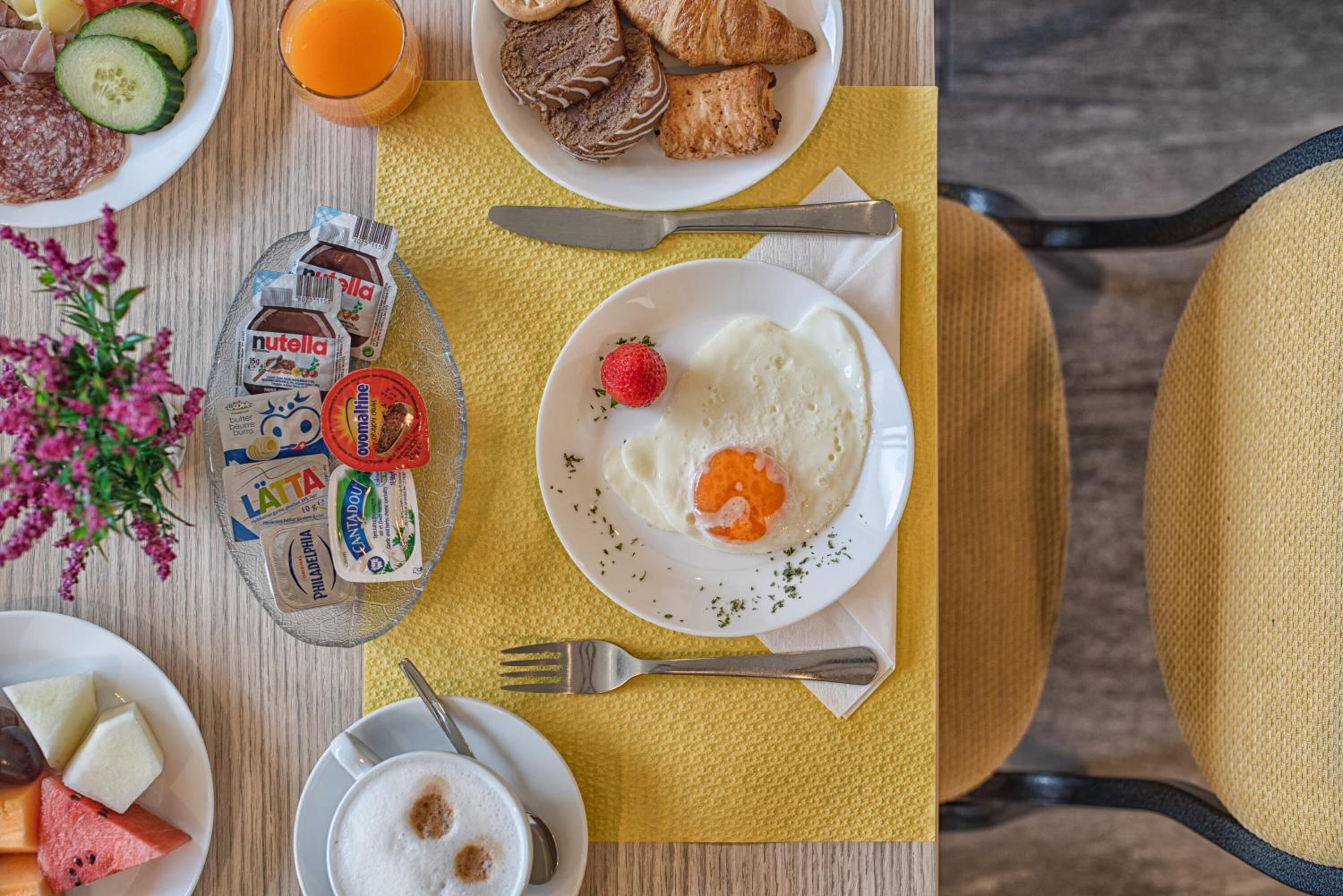 A breakfast setting with a plate of scrambled eggs, a strawberry, and a glass of orange juice.