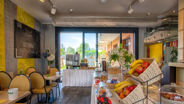 Un bufé de desayuno con diversas frutas y pasteles, una pizarra con un mensaje y vistas al exterior.