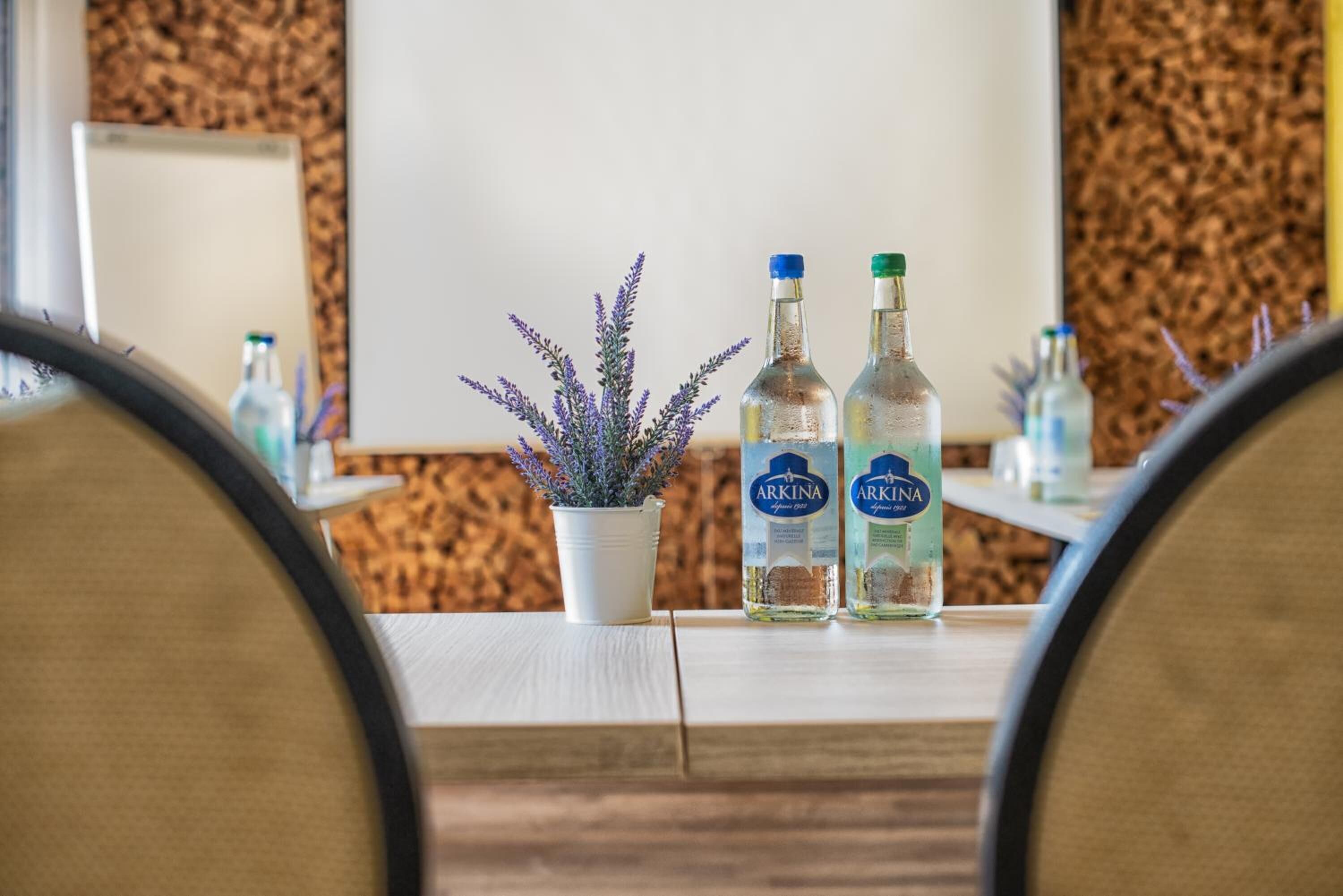 A conference table with two bottles of Arkina vodka, a potted lavender plant, and a whiteboard in a room with cork wall decor.