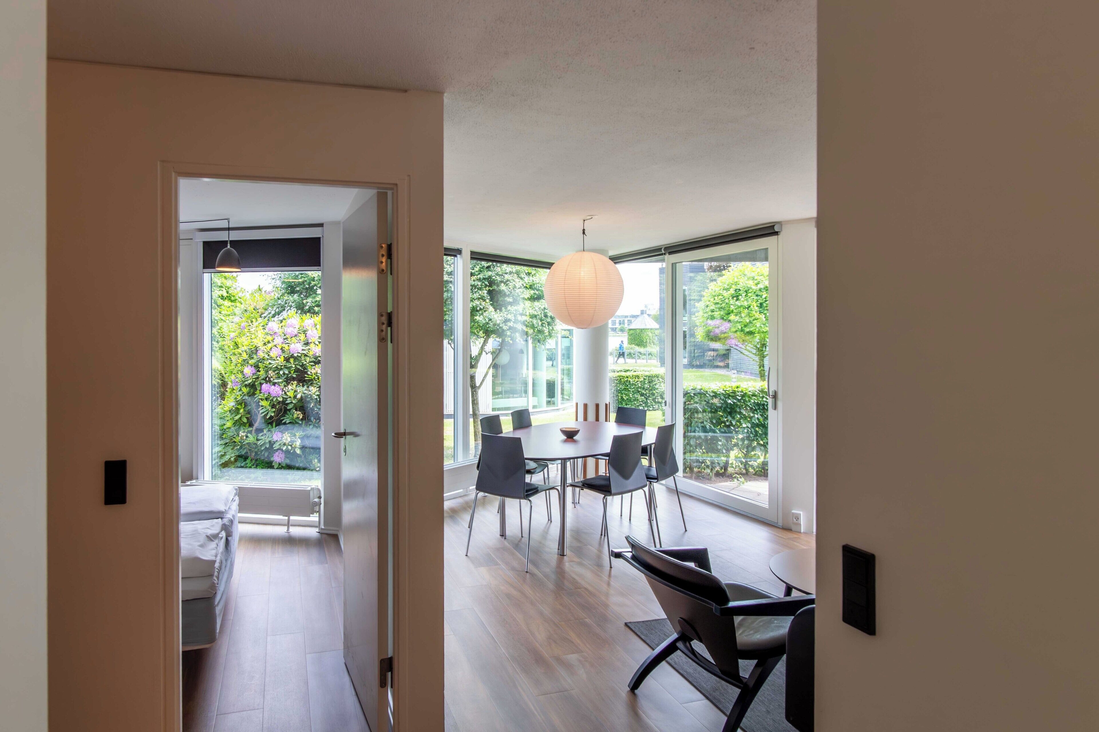 A modern interior with a dining area, large windows, and a view of greenery.