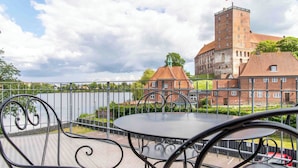 Uma varanda com mesa e cadeiras de metal, com vista para um corpo de água e um edifício histórico com torre.