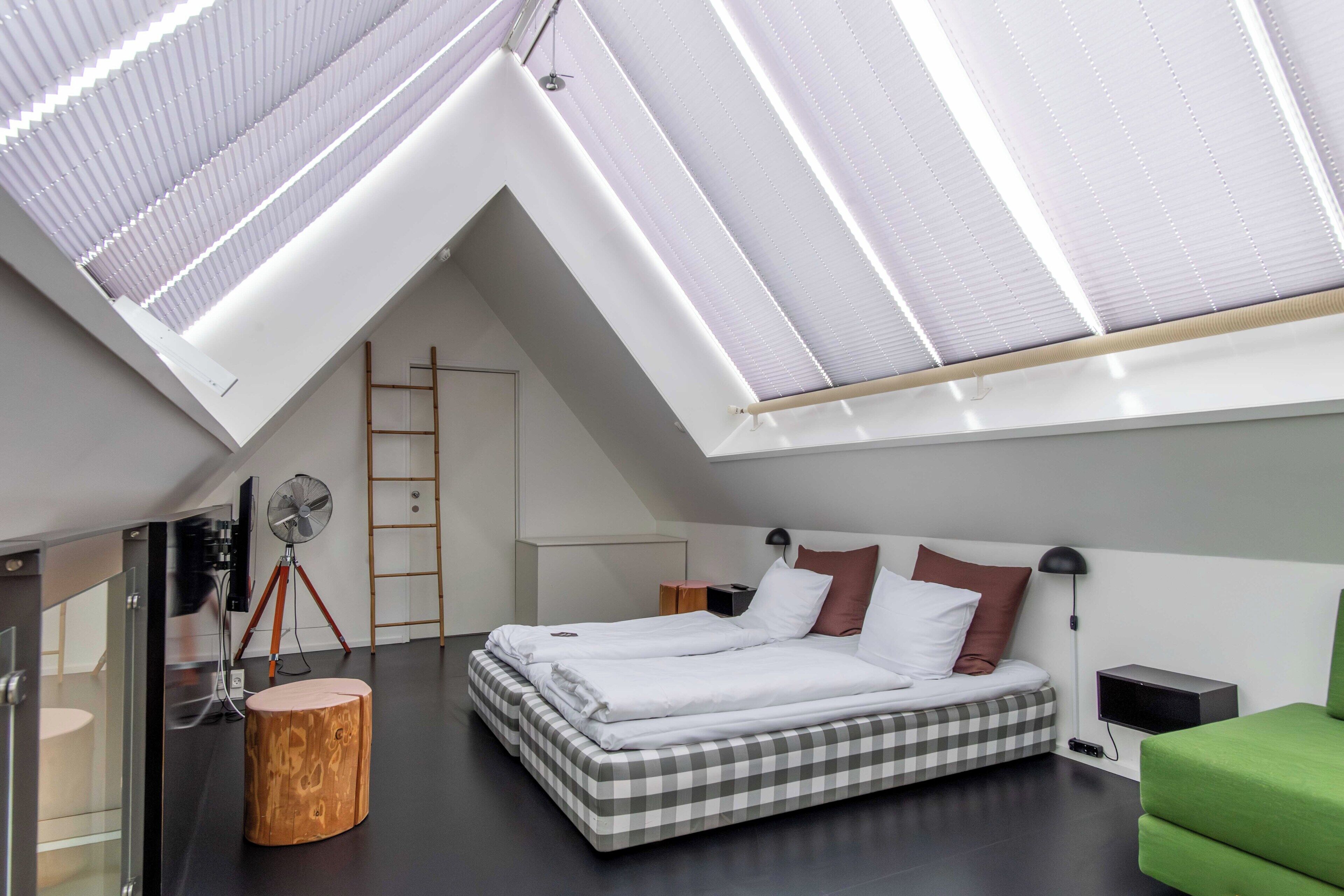 Een moderne slaapkamer met dakraam, een bed met geruit beddengoed, een groene stoel en een houten kruk.