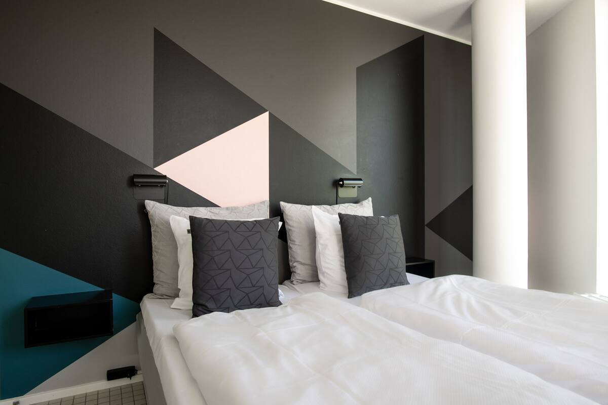 A modern hotel room with a large bed, geometric wall design, and bedside lamps.