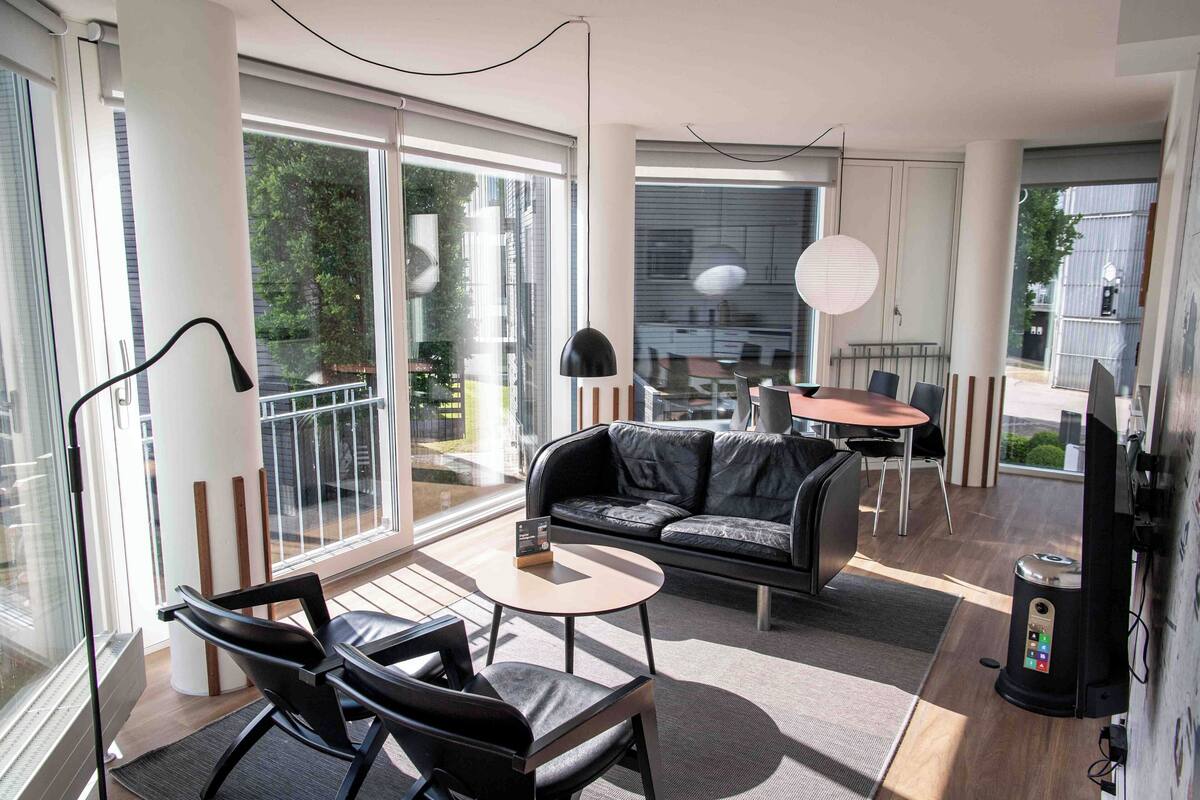 A modern living room with a sofa, chairs, a small table, and a TV.