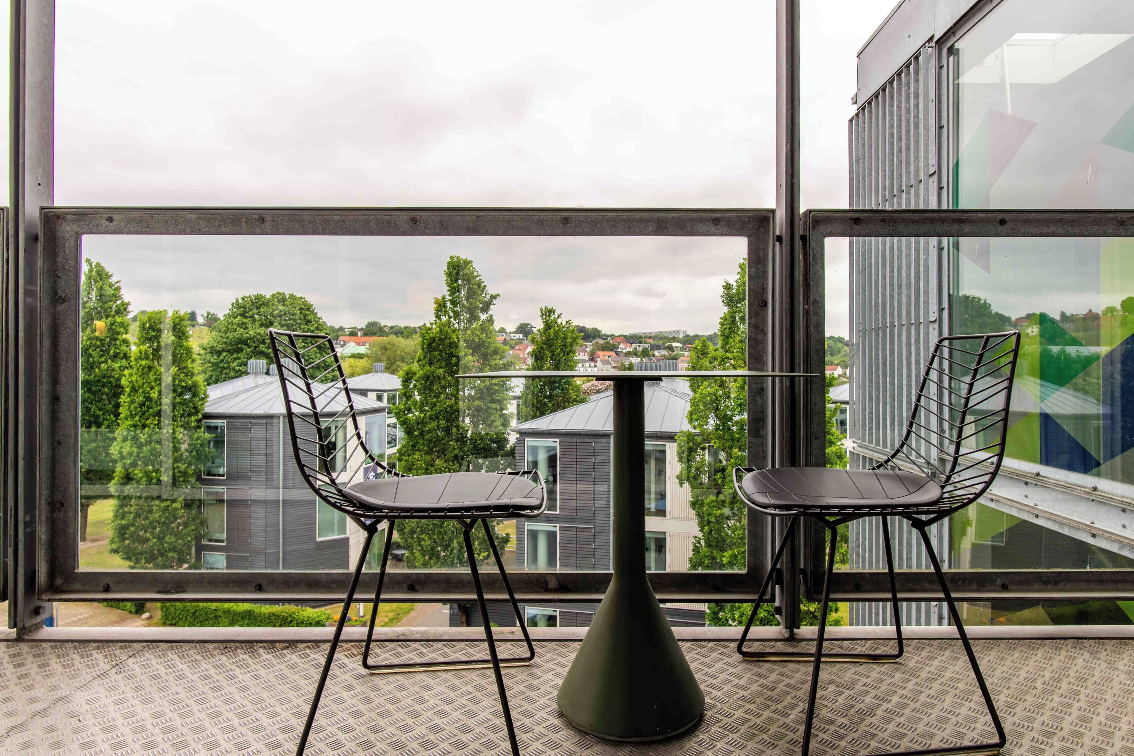 A room with a large window, two chairs, a small table, and a modern floor pattern.