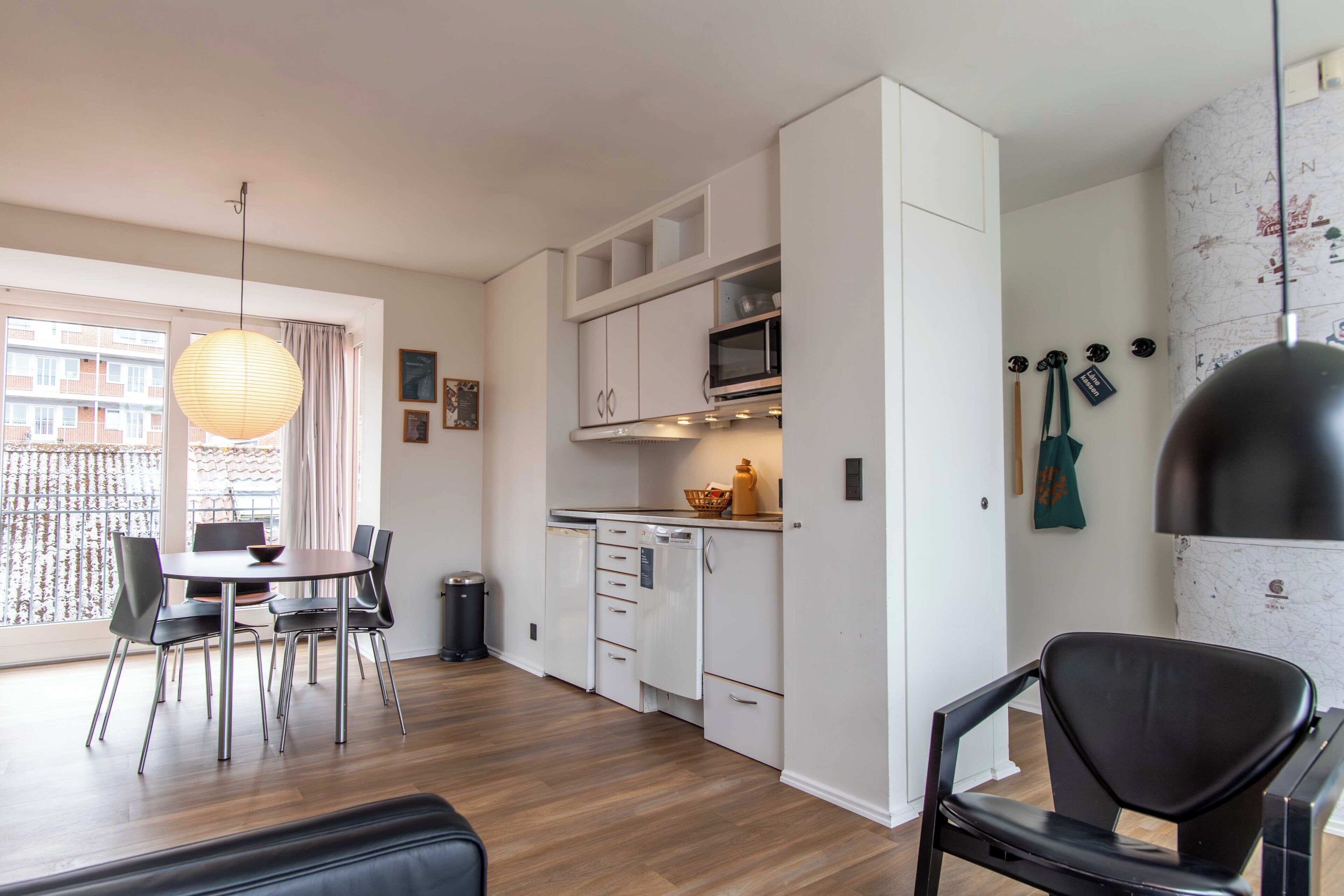 A modern kitchen with white cabinets, a microwave, and a black grill. There is a dining table with chairs and a hanging light fixture.