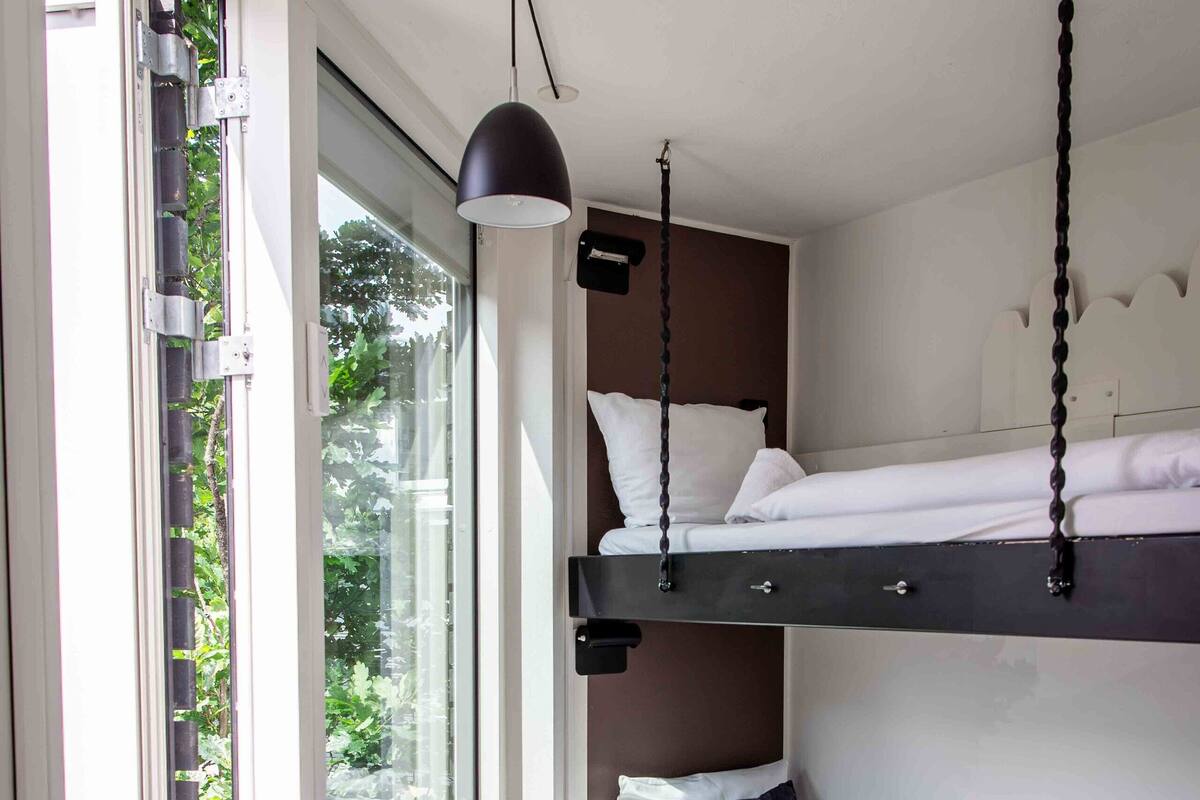A modern room with a large window, a radiator, a hanging light fixture, and a bunk bed.