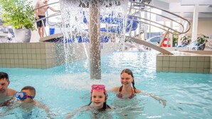 Piscina interior com um elemento aquático, paredes azulejadas e um escorrega visível ao fundo.