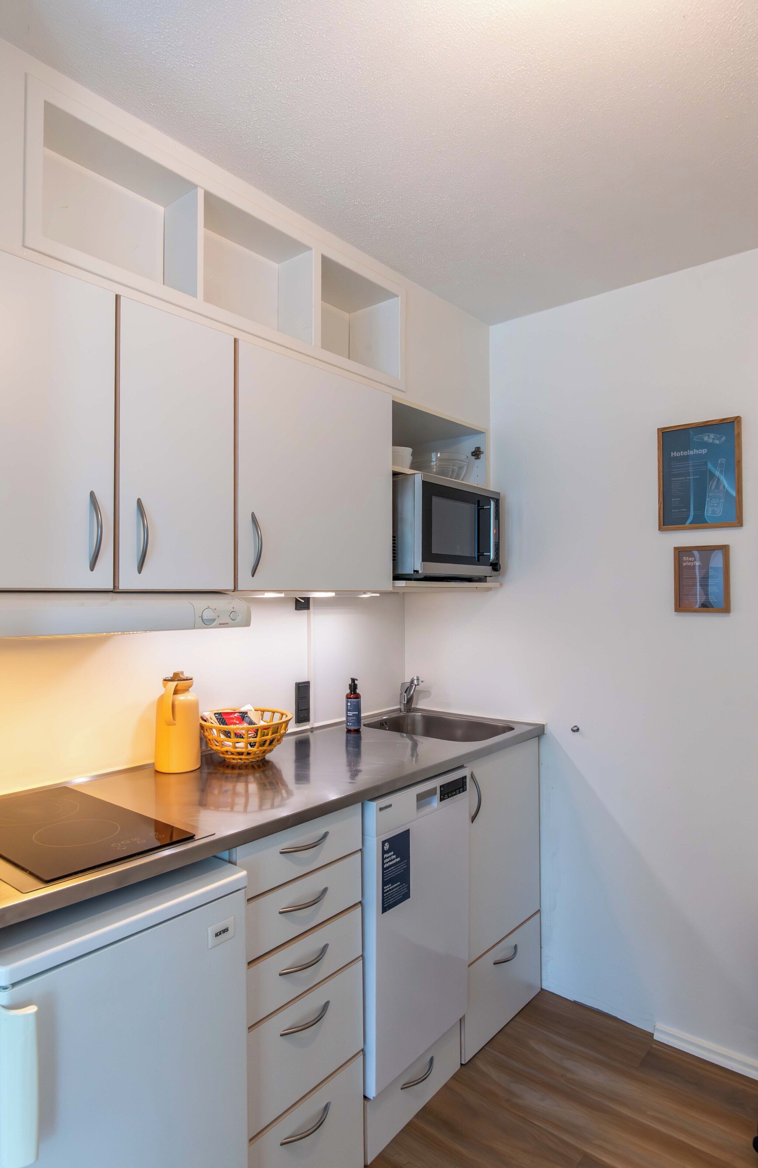 A compact kitchen with white cabinets, a microwave, a sink, and a small refrigerator.
