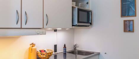 A compact kitchen with white cabinets, a microwave, a sink, and a small refrigerator.
