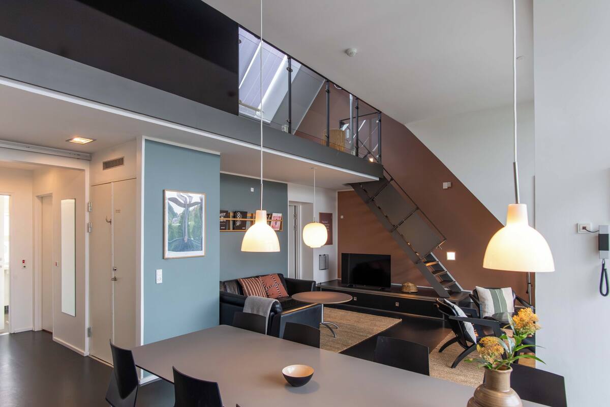 A modern living space with a dining area, sofa, TV, staircase, and a view of the outdoors.