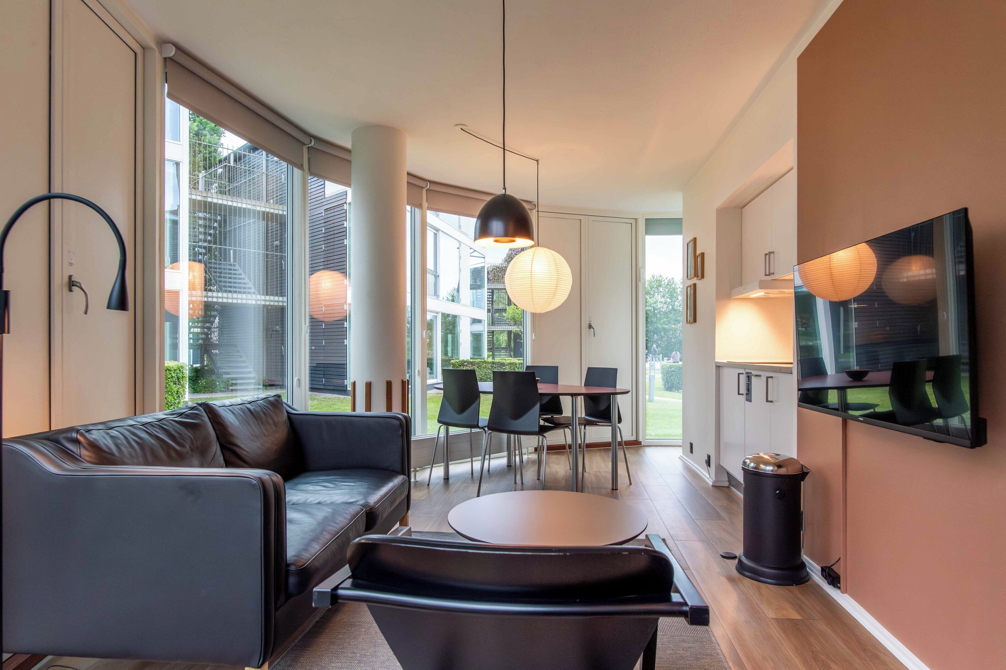 A modern living room with a sofa, a dining table, chairs, and a TV mounted on the wall.
