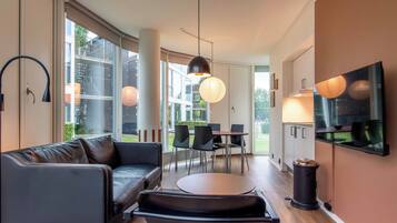 A modern living room with a sofa, a dining table, chairs, and a TV mounted on the wall.