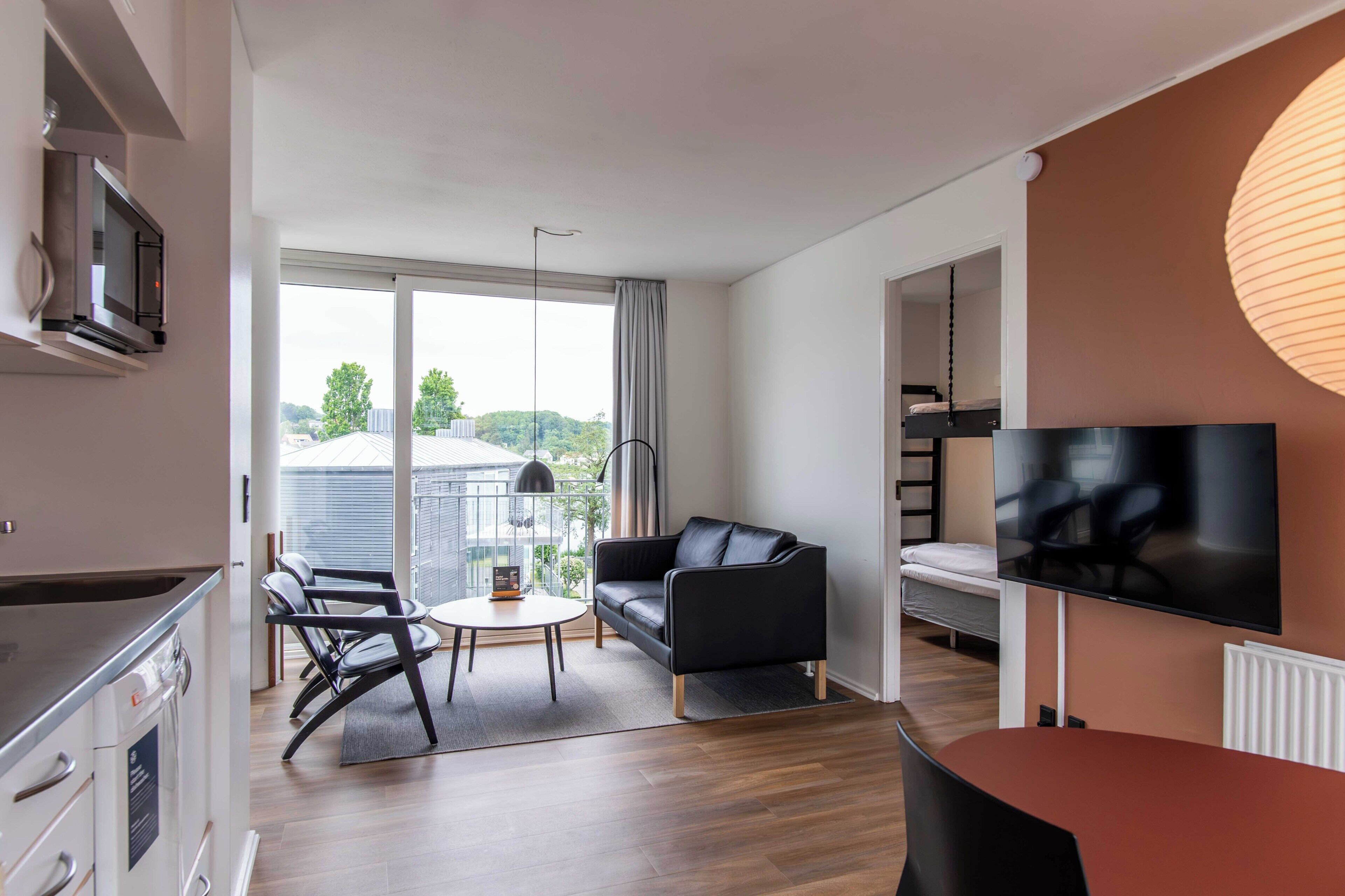 Ein modernes Wohnzimmer mit einer Couch, einem Fernseher und einem Essbereich mit Tisch und Stühlen.