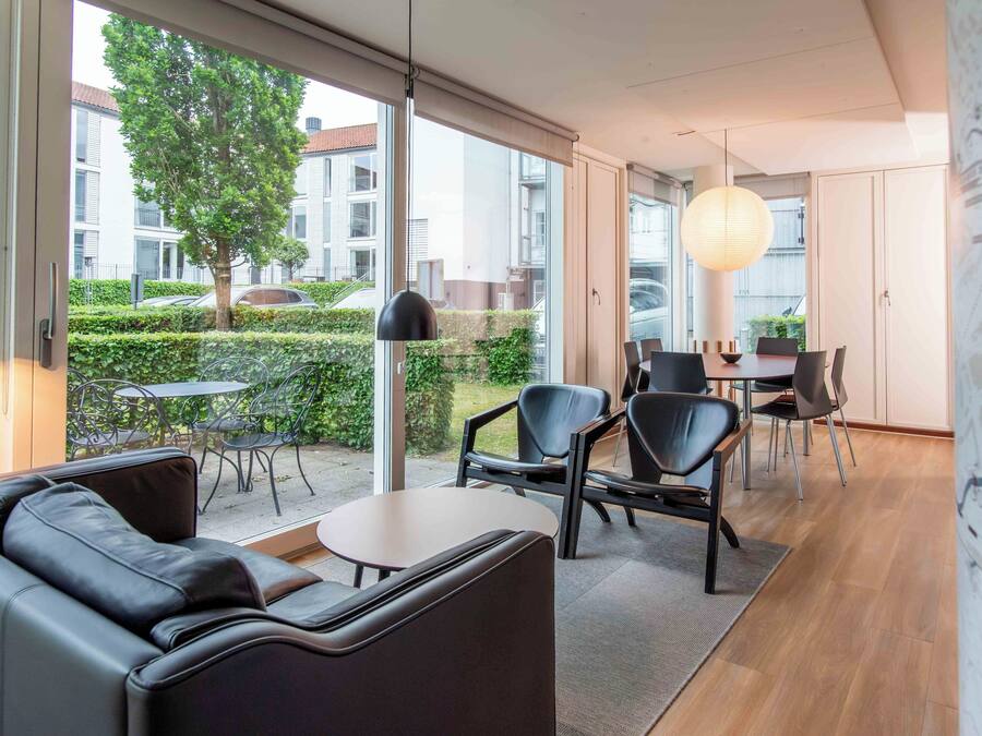 A modern interior with a sofa, chairs, a table, and a view of the outside.