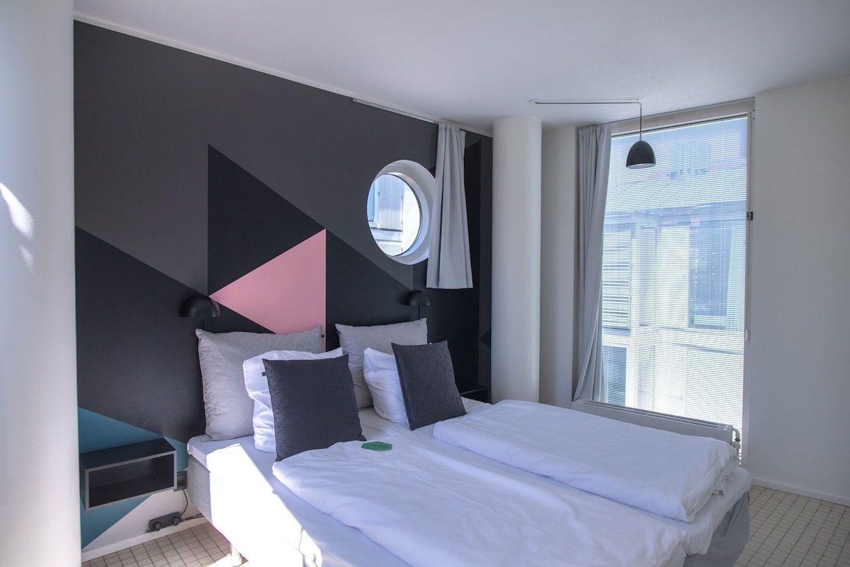 Una habitación de hotel moderna con una cama, un ventanal redondo y vistas a la ciudad.
