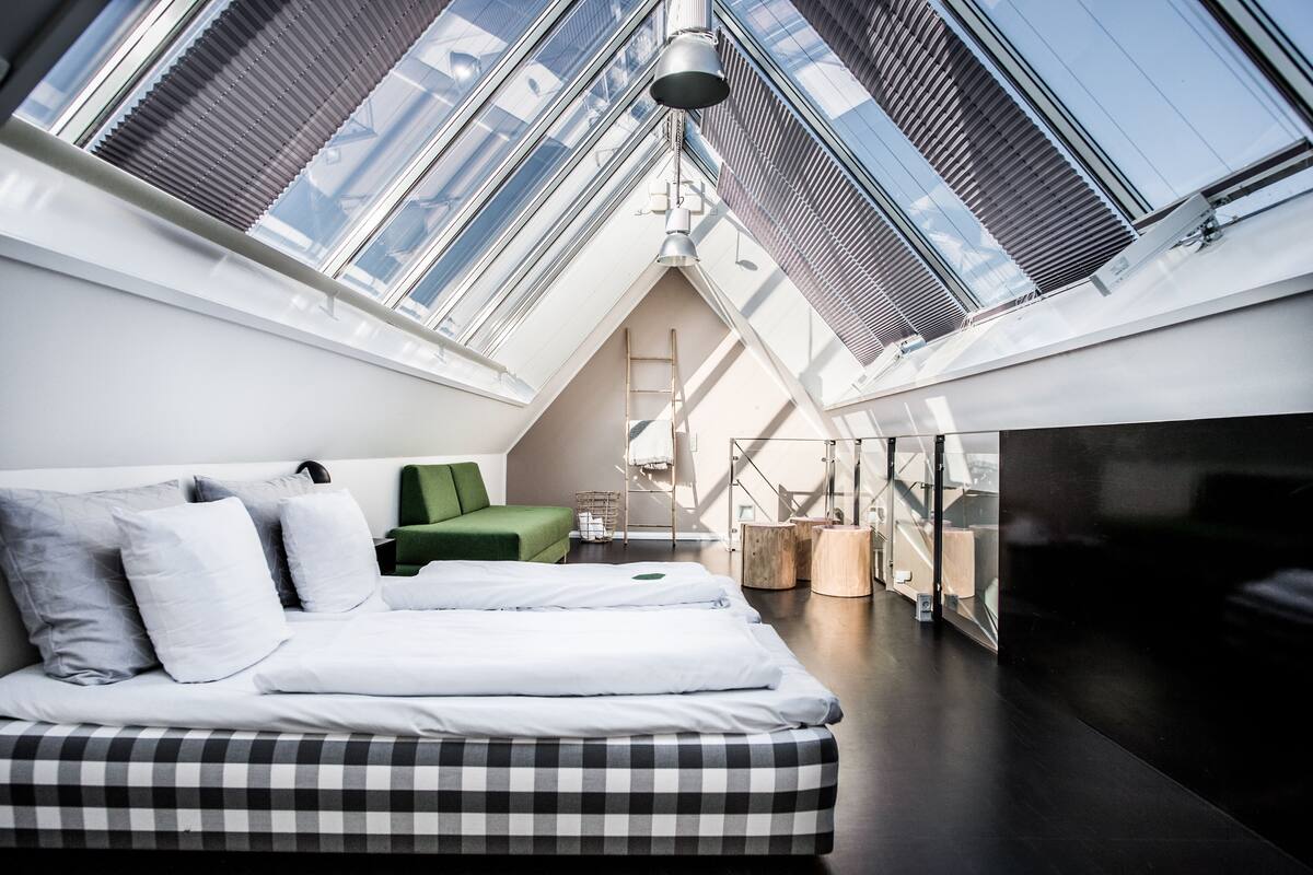A modern loft bedroom with skylights, a bed, a green chair, and a wooden side table.