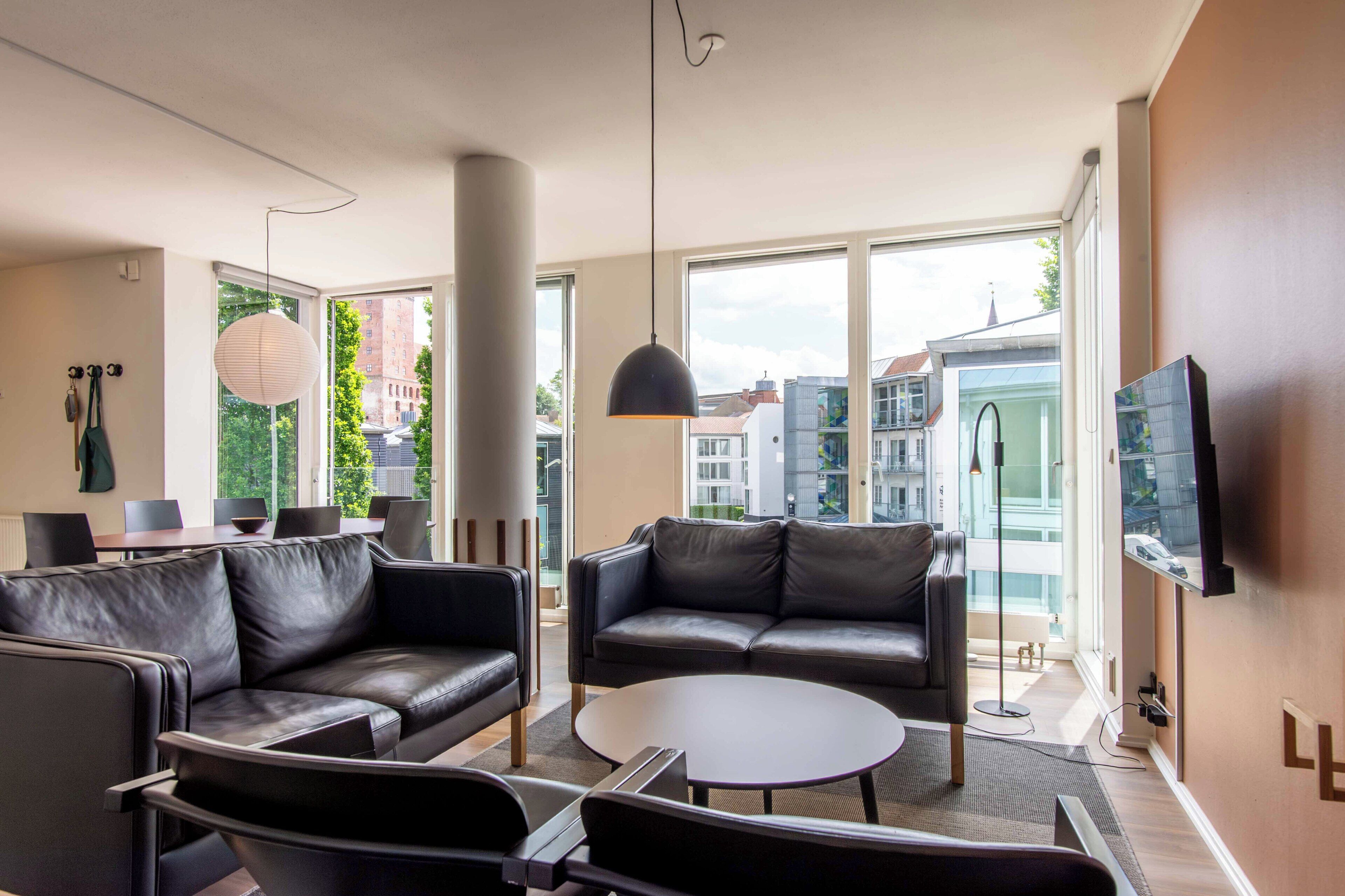 Un salon moderne avec des canapés en cuir, une table basse ronde et une grande fenêtre donnant sur la ville.