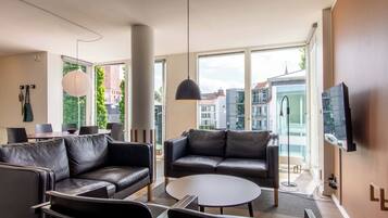 Un salon moderne avec des canapés en cuir, une table basse ronde et une grande fenêtre donnant sur la ville.