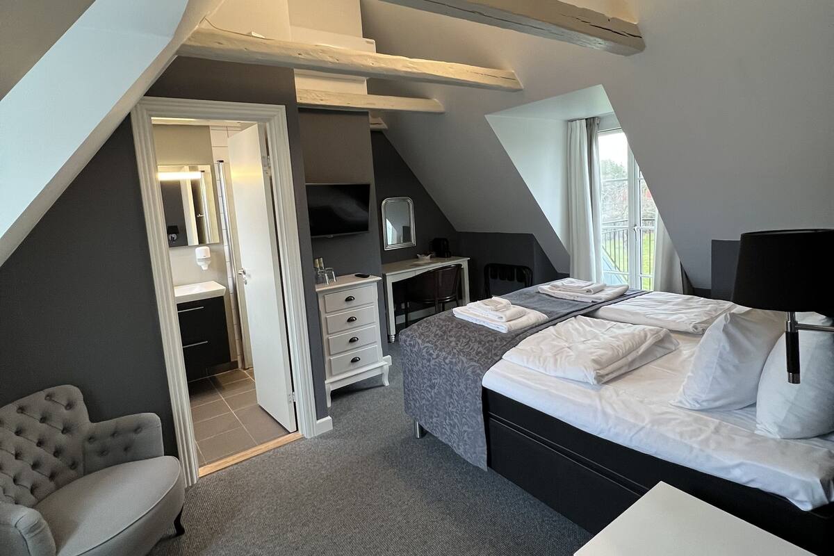 Une chambre avec un plafond en pente, un lit, une chaise, un bureau et un téléviseur.