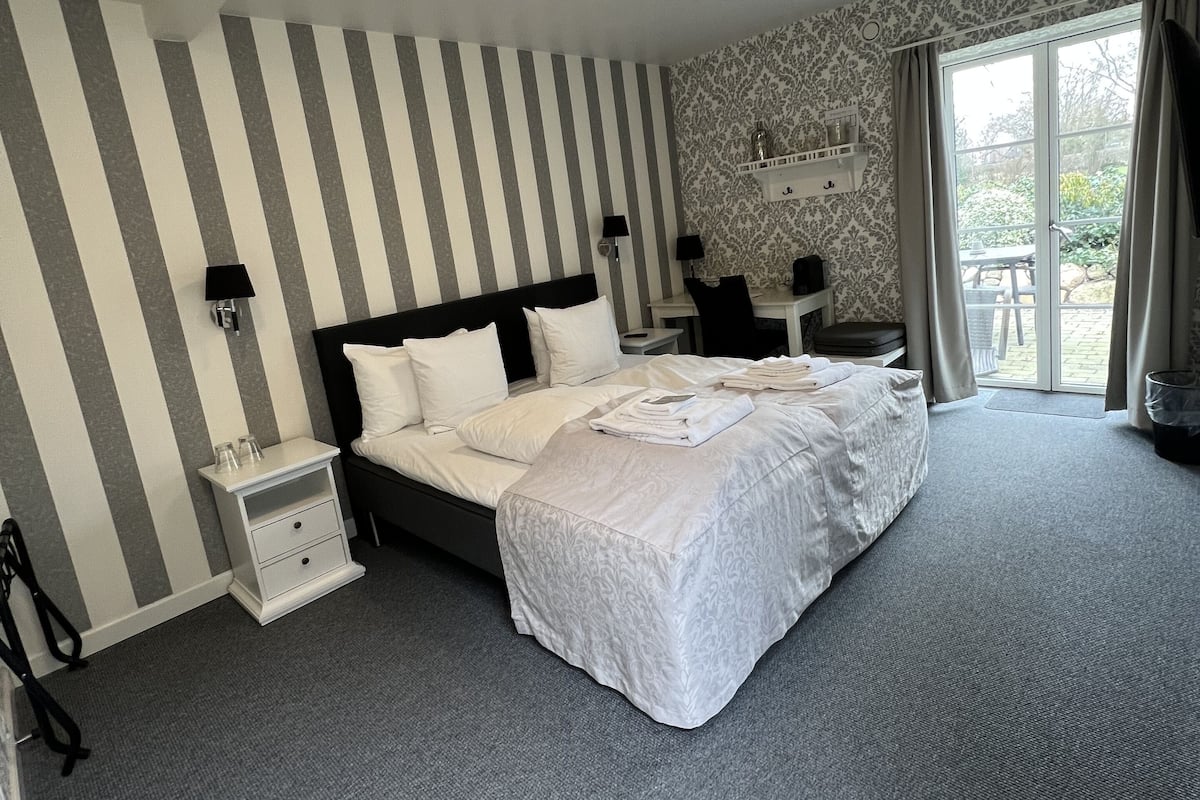 Une chambre d’hôtel avec un grand lit, une table de chevet, un bureau et une fenêtre avec des rideaux.