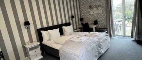 Quarto de hotel com uma cama grande, mesa de cabeceira, escrivaninha e janela com cortinas.