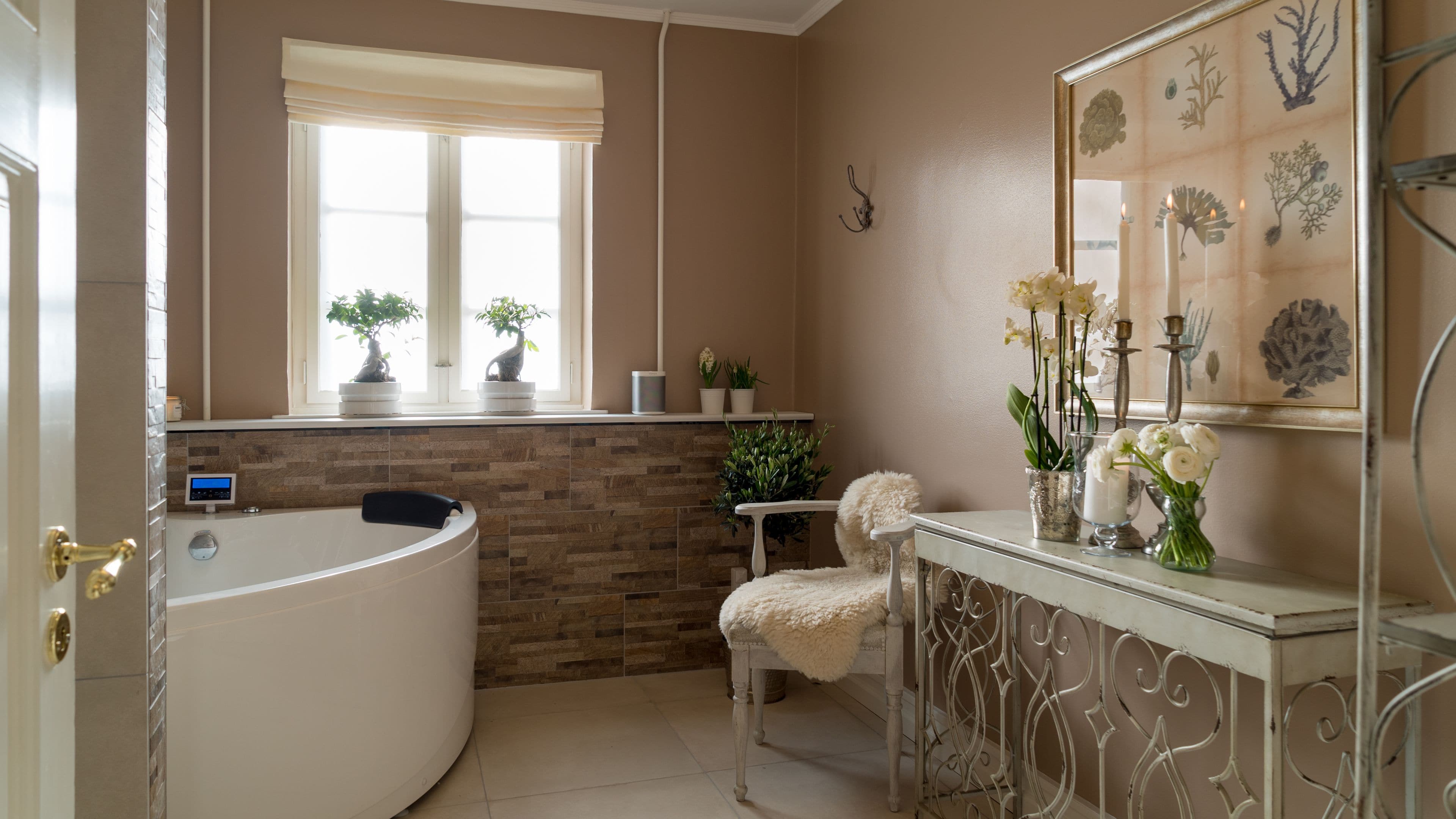 A bathroom with a large bathtub, a vanity with a mirror, and a window with potted plants.