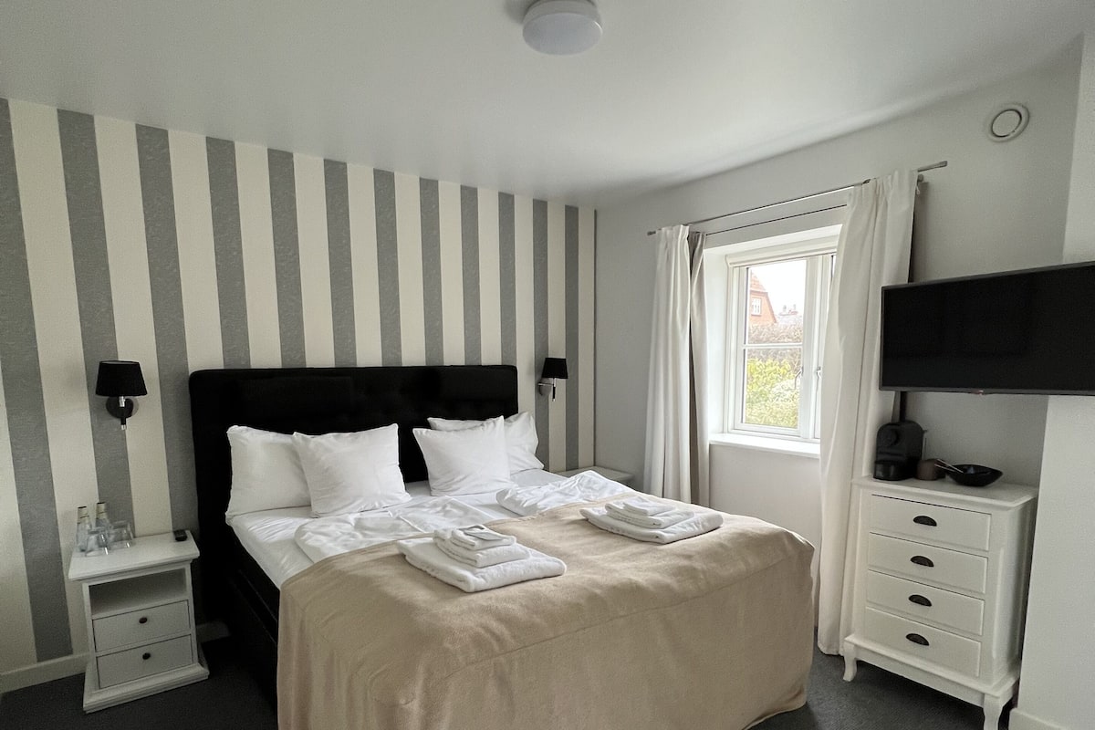 Une chambre bien rangée, avec un lit, des tables de chevet, une télévision et une fenêtre avec des rideaux.