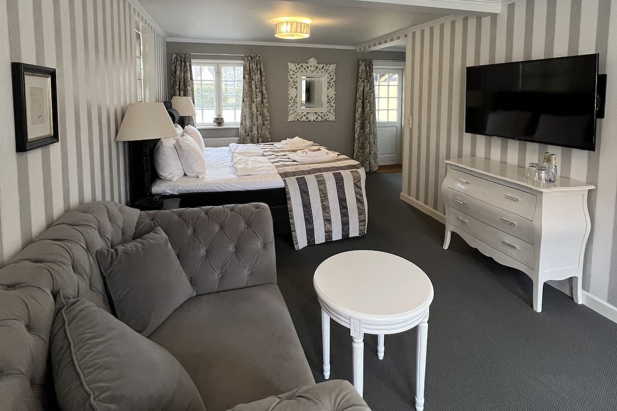 Une chambre d’hôtel avec un grand lit, un canapé, une petite table, une commode et un téléviseur.
