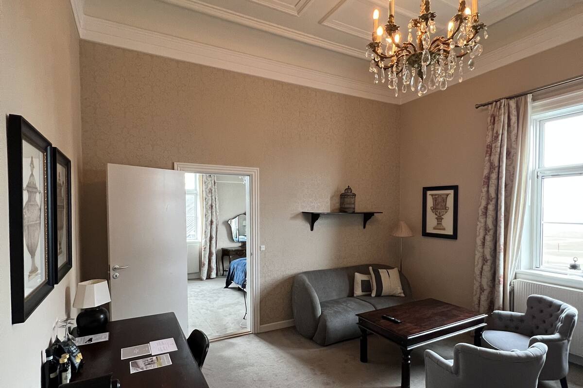 Un salon avec un lustre, un canapé, des fauteuils, une table basse et une table à manger.
