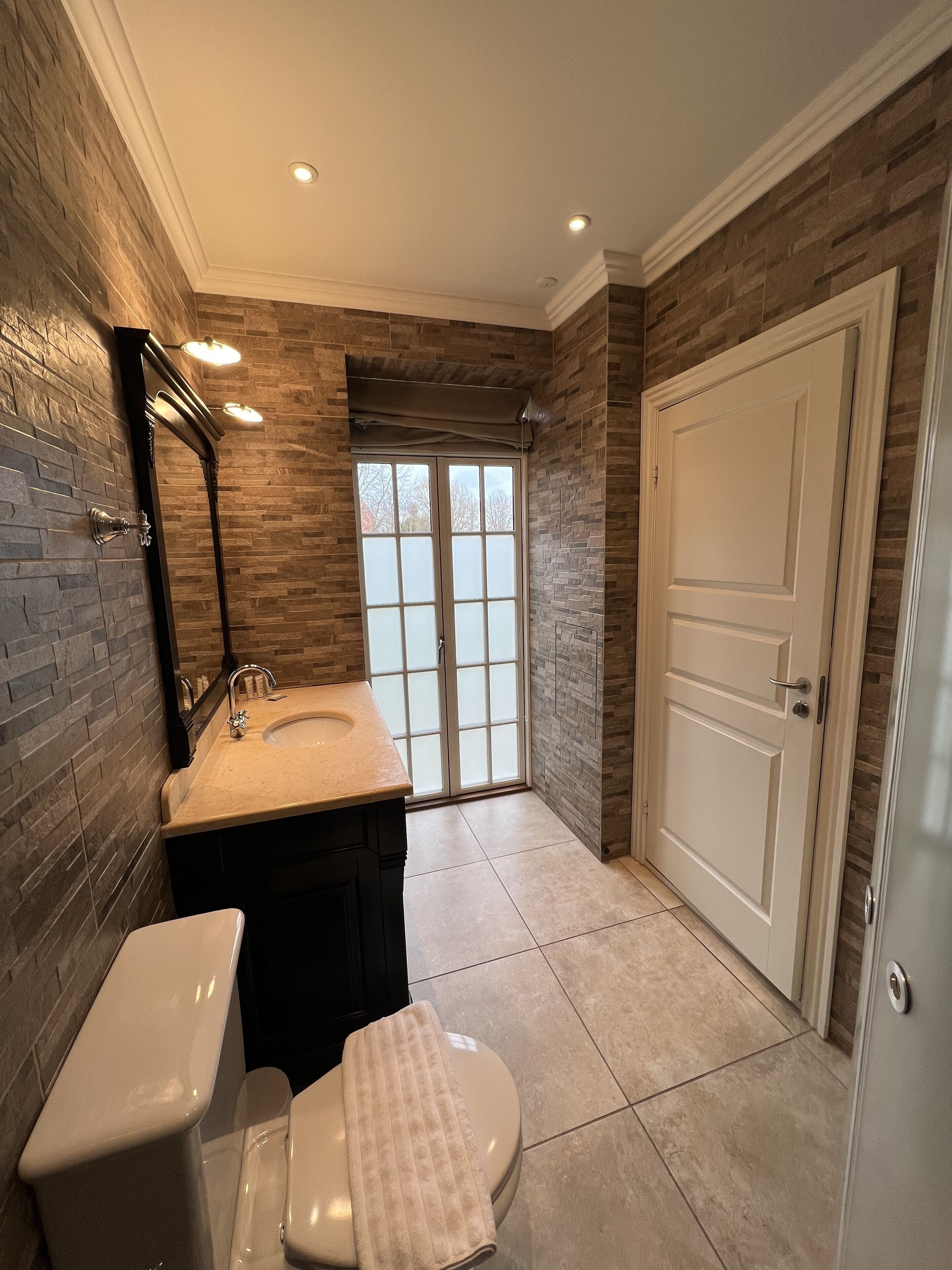 Een badkamer met een grote spiegel, een wastafel, een toilet en een deur.