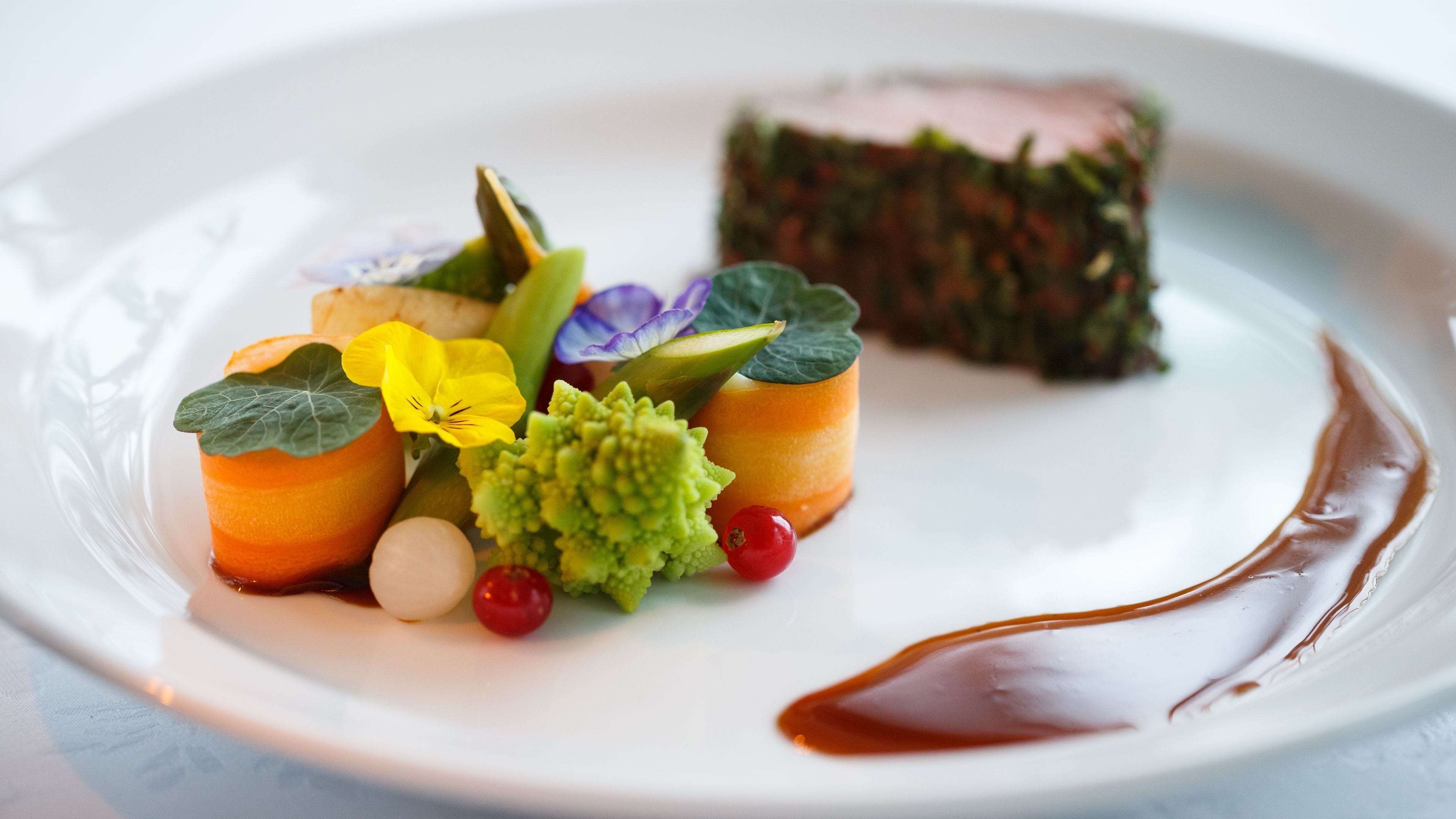 A white plate with a dish of food, including a piece of meat, vegetables, and a sauce.