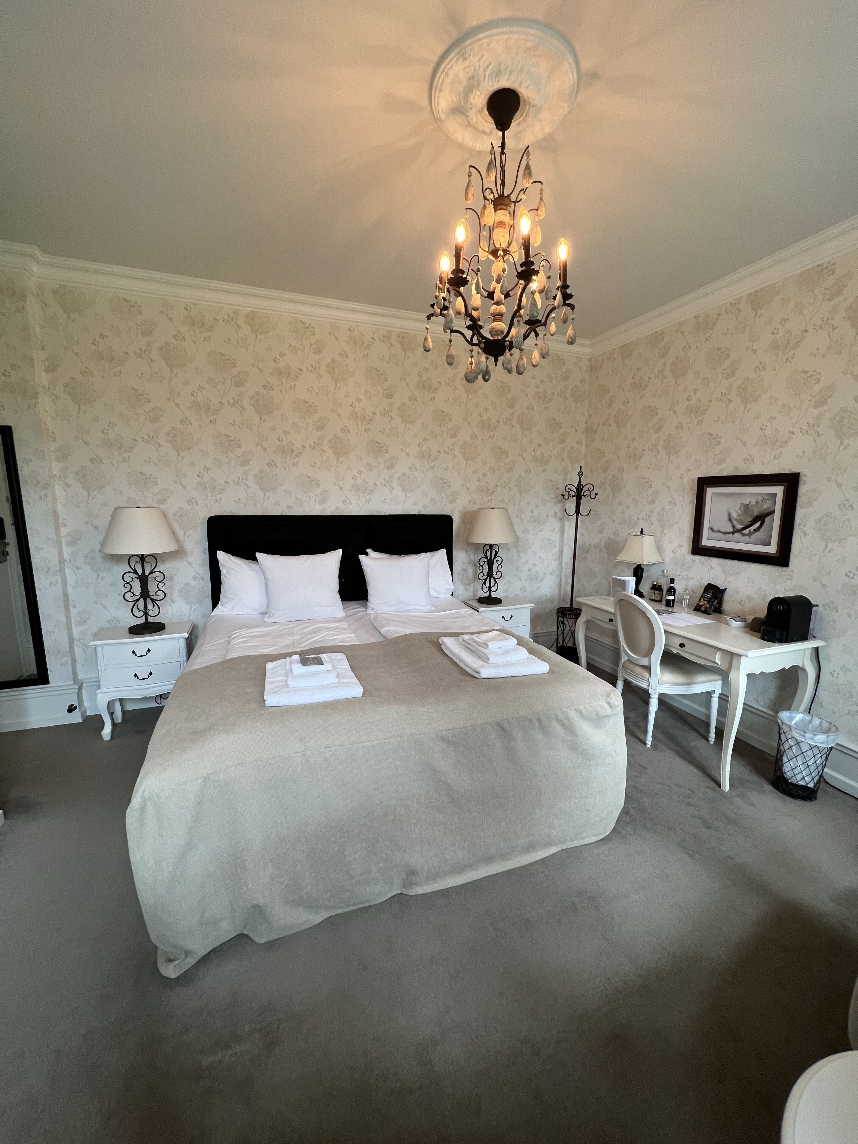 A spacious bedroom with a large bed, two bedside tables, a desk, and a chair.