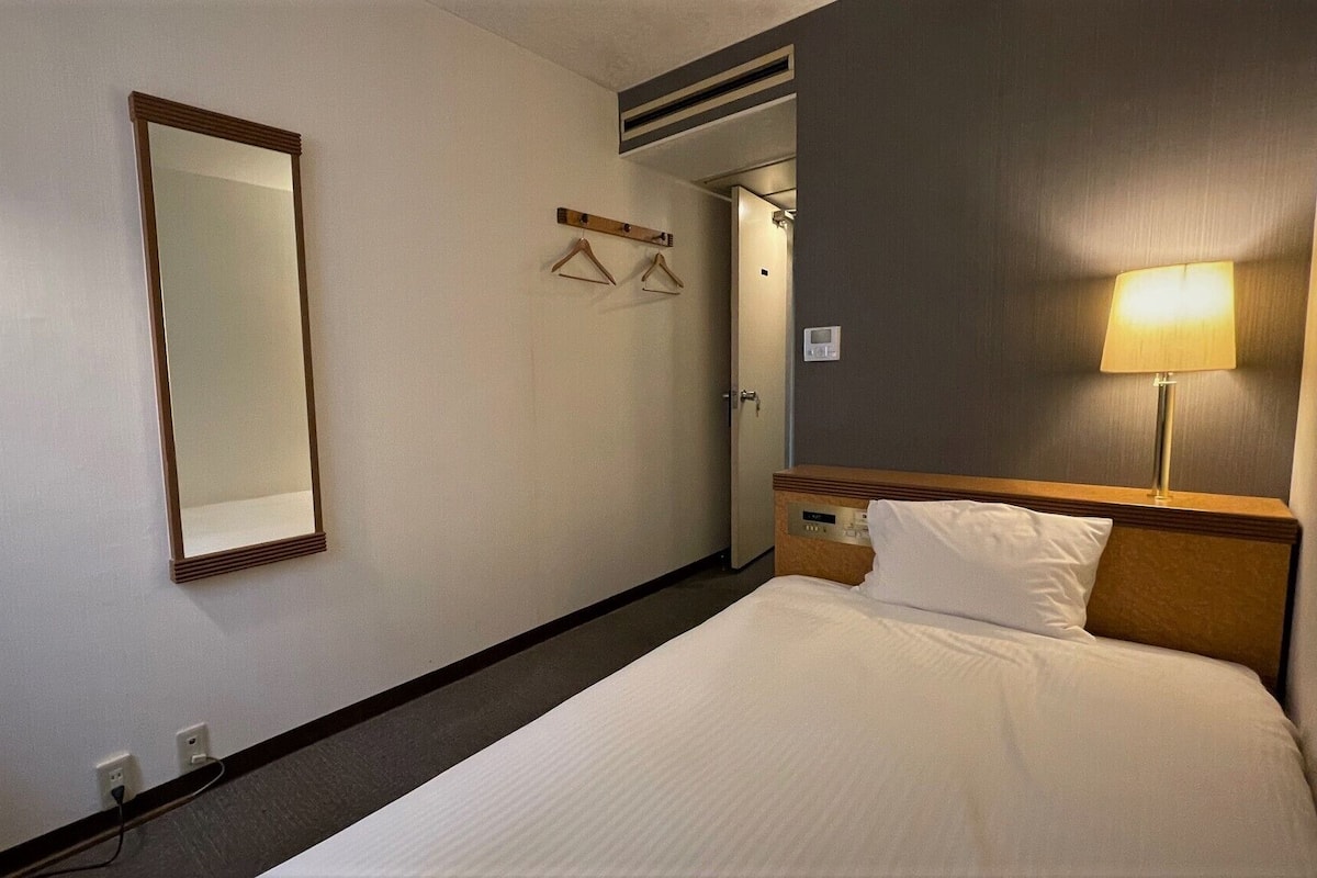 Una camera d'albergo con un letto, una lampada da comodino, uno specchio e un appendiabiti.