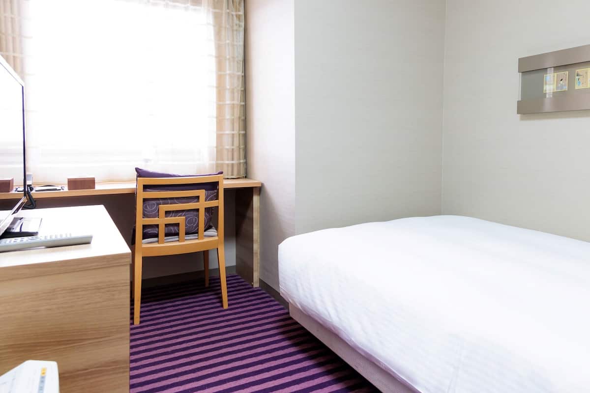 A hotel room with a bed, a desk with a computer, a chair, and a window with curtains.