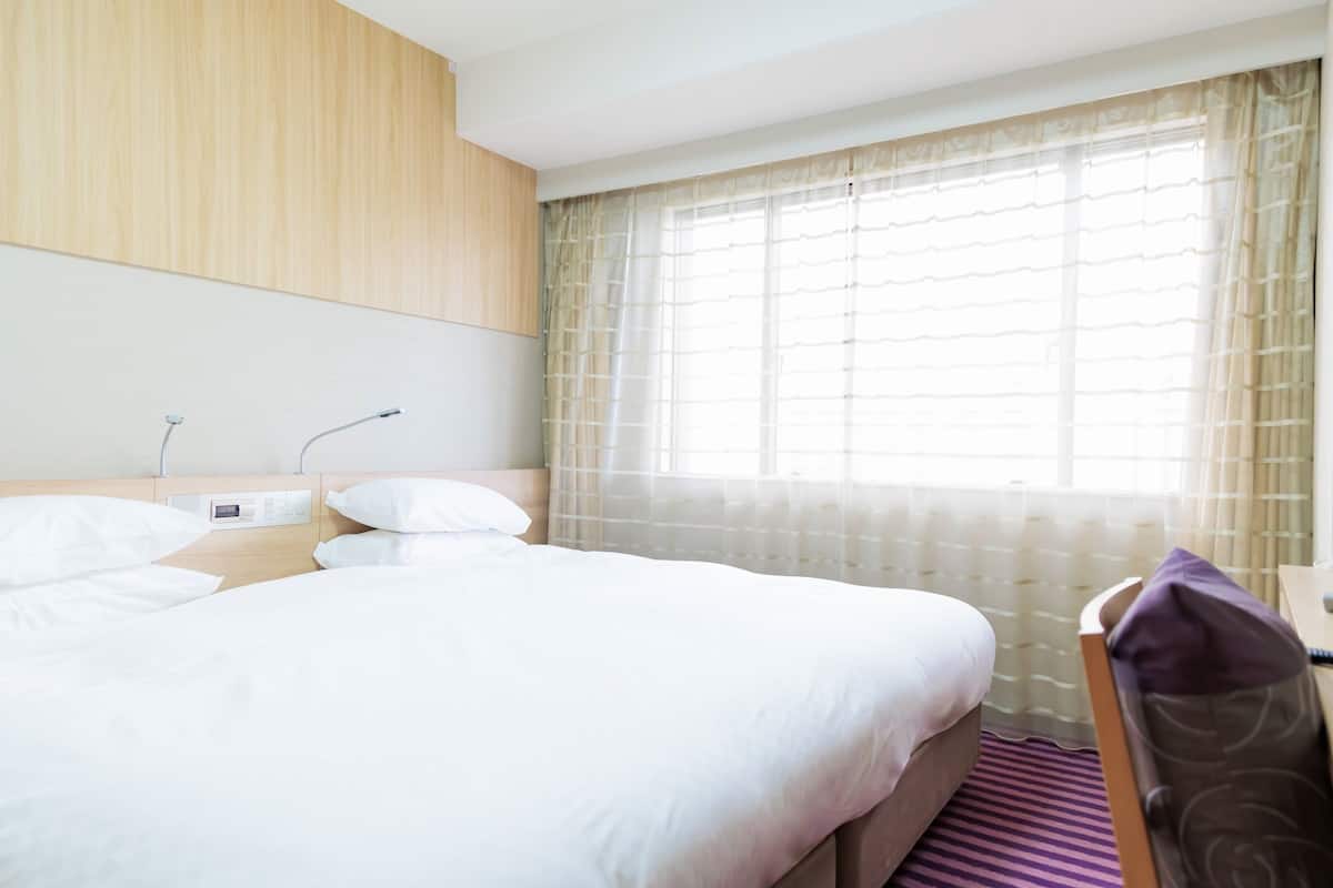A hotel room with a bed, bedside table, lamp, and window with curtains.