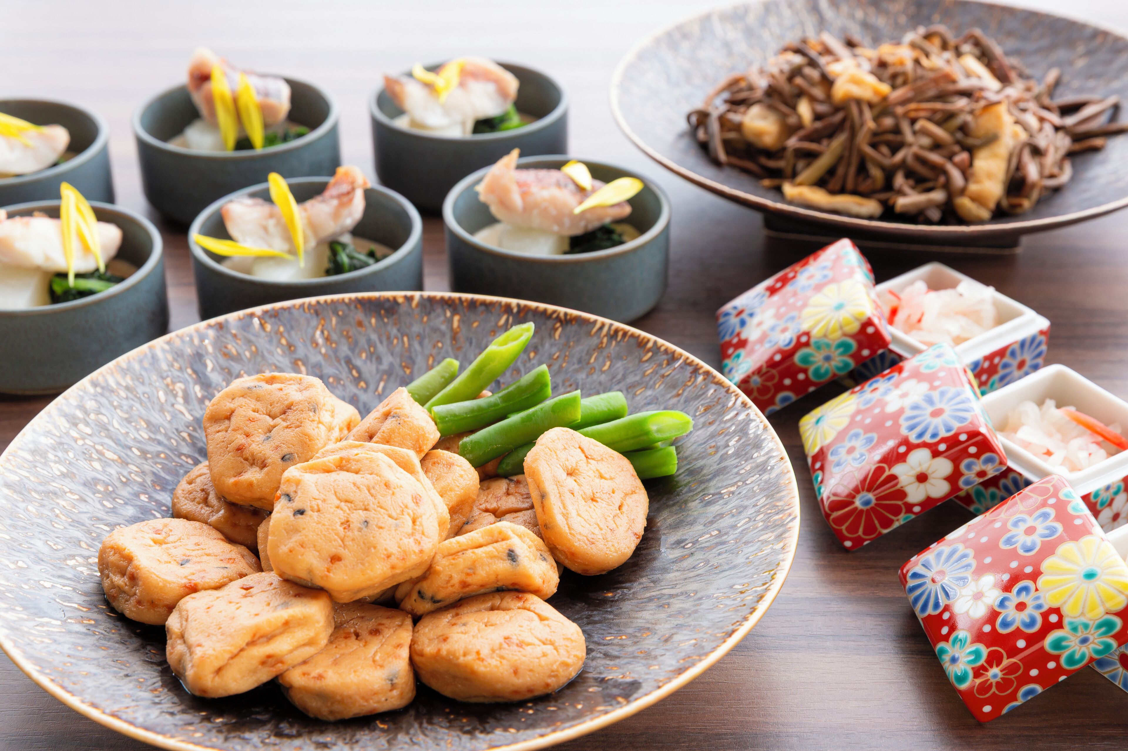 A variety of dishes including a bowl of green vegetables, a plate of round cookies, and several small cups with food items.