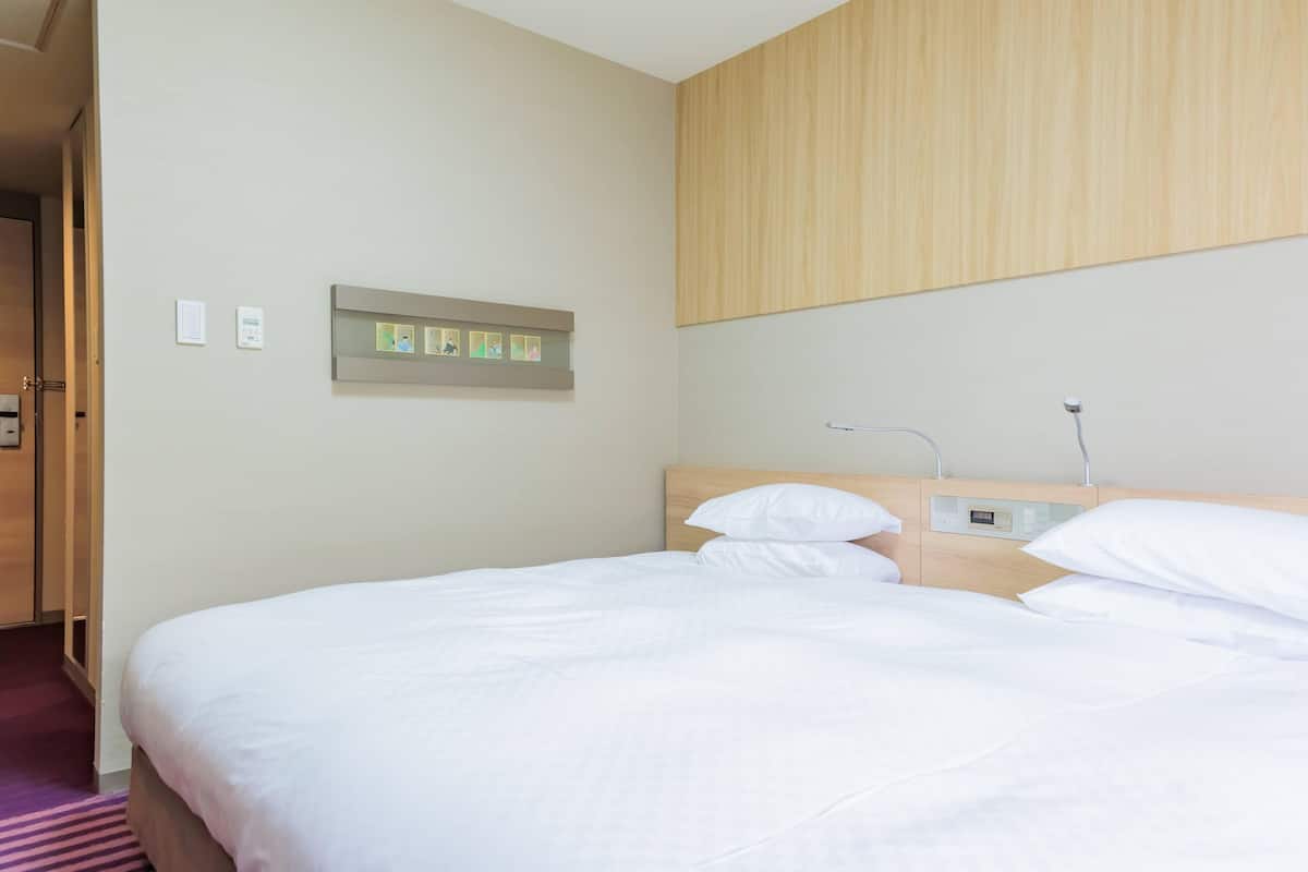 A hotel room with a bed, a wooden headboard, a control panel, and a wall-mounted light fixture.
