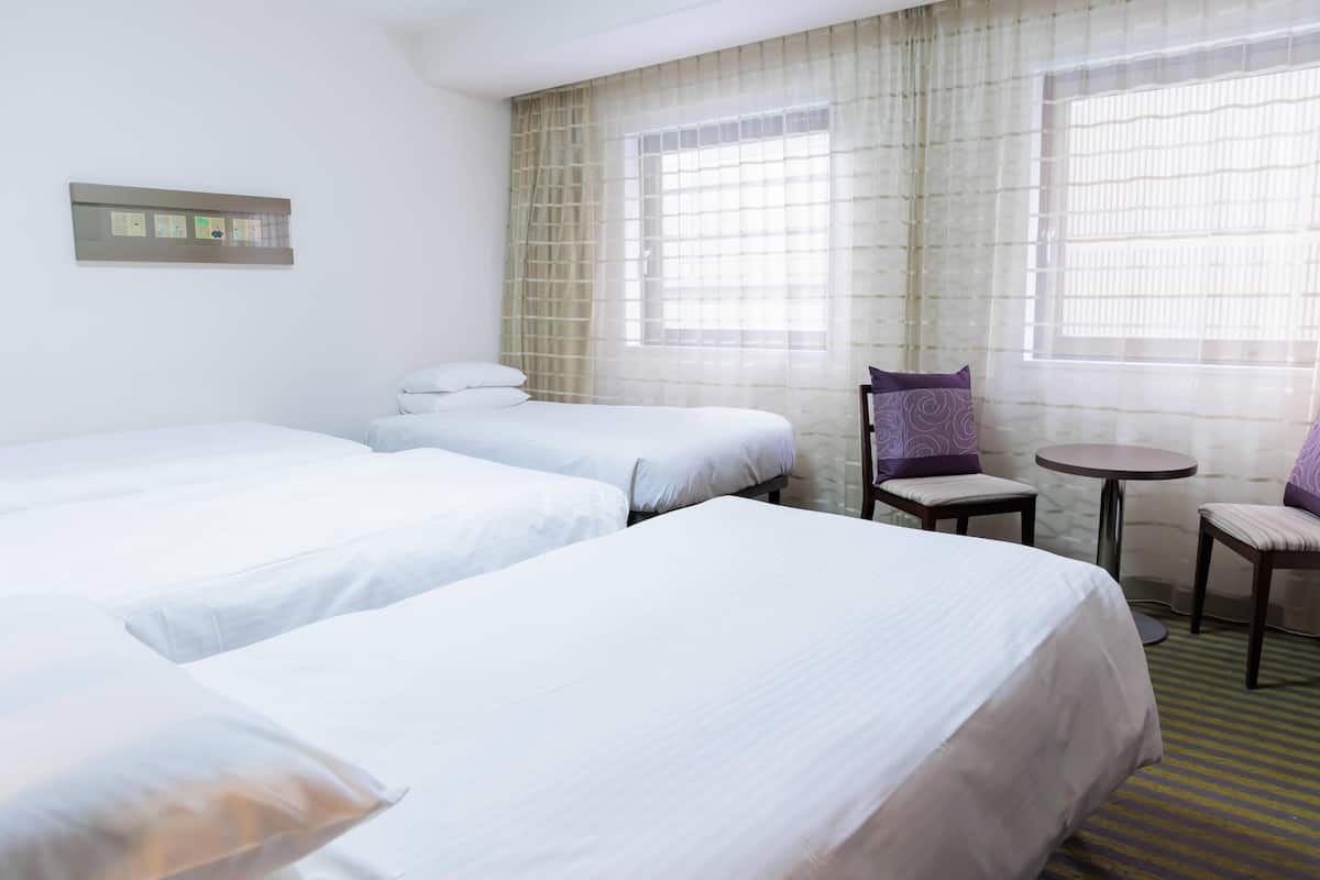 A hotel room with two single beds, a small round table, two chairs, and a window with sheer curtains.