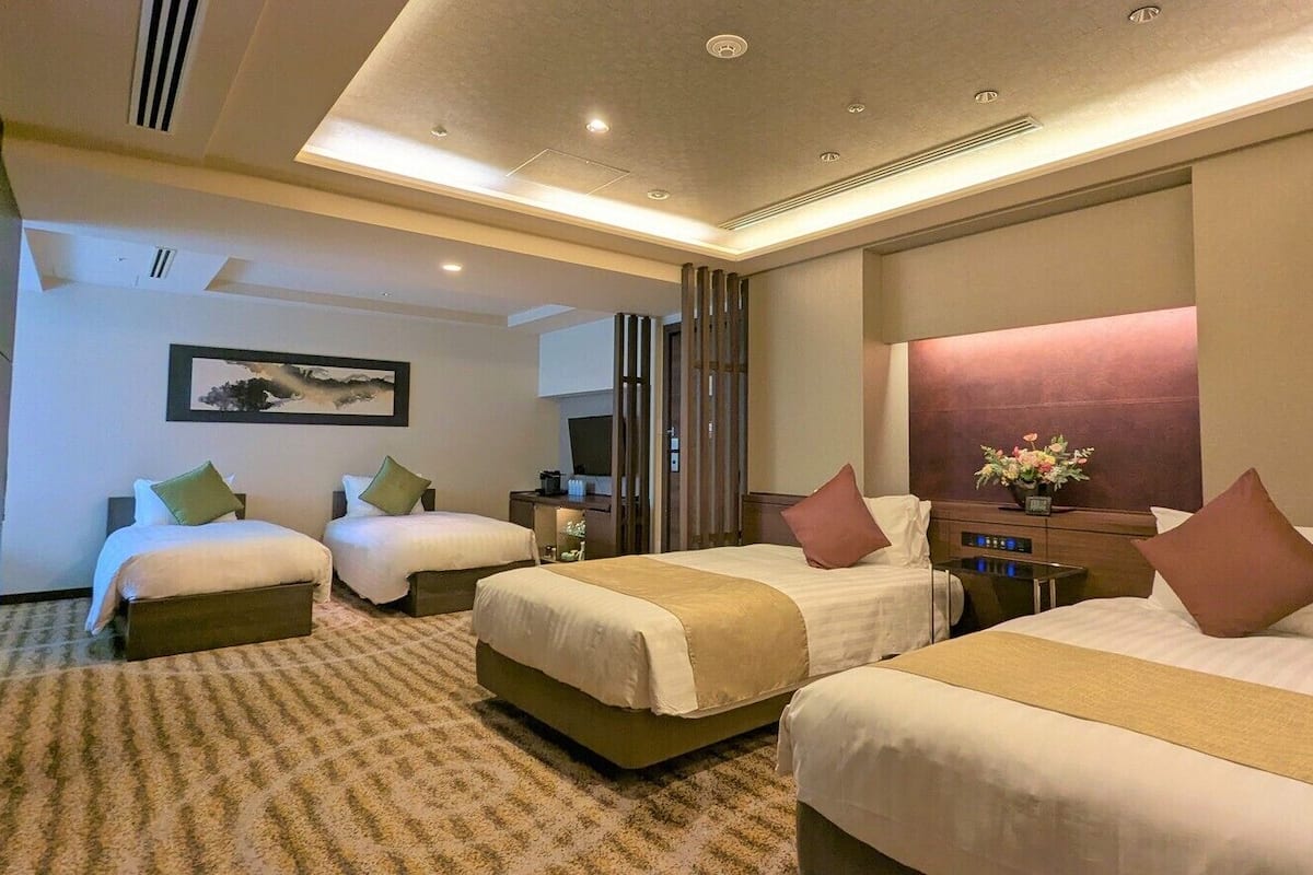 A hotel room with three beds, a television, a desk with a computer, and a large window.