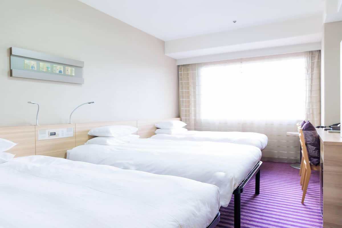 A hotel room with three beds, a desk, a chair, and a window with curtains.