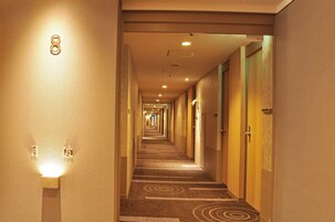 A hotel hallway with a carpeted floor, wooden doors, and a light fixture on the wall.