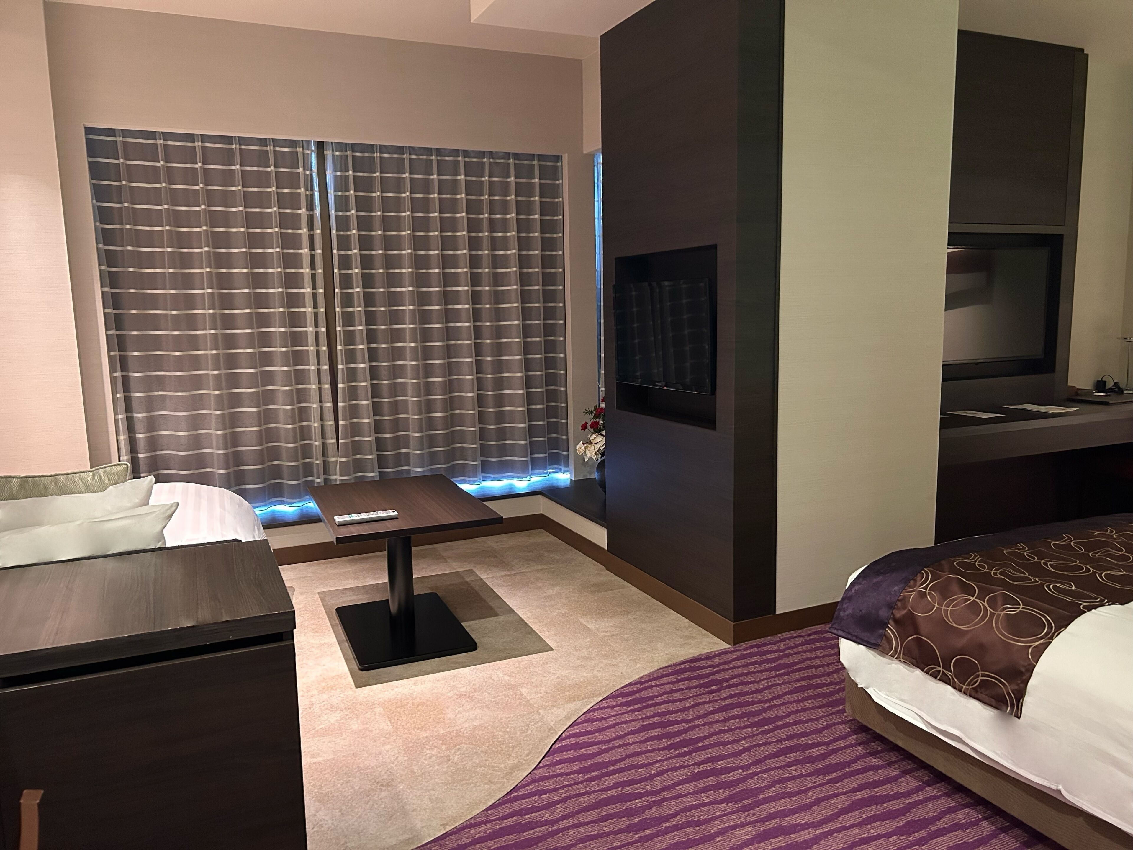 A hotel room with a bed, a desk, a TV, and a window with curtains.