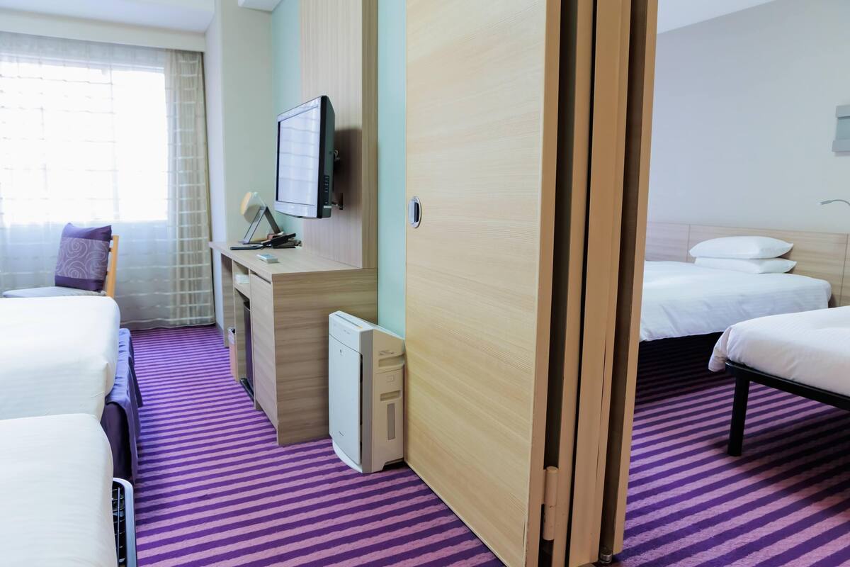A hotel room with two beds, a desk with a computer, a TV, and a window with curtains.