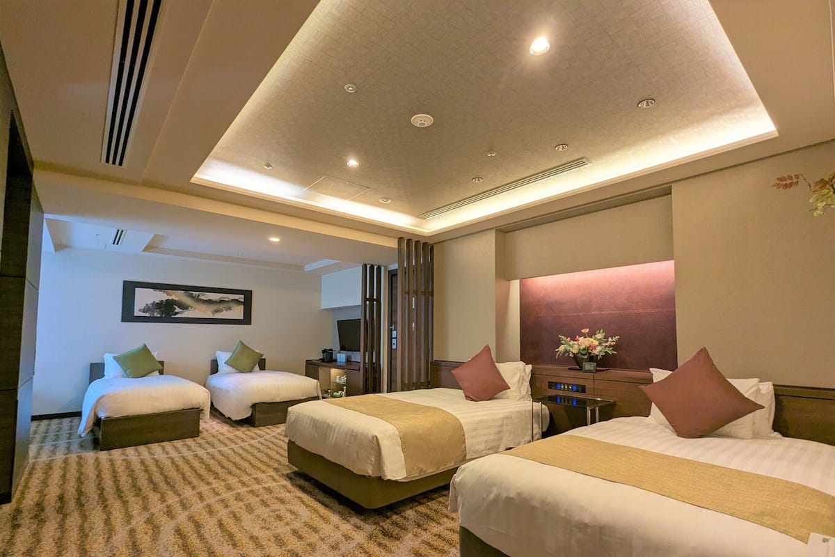 A hotel room with two beds, a TV, a desk, and a bathroom.