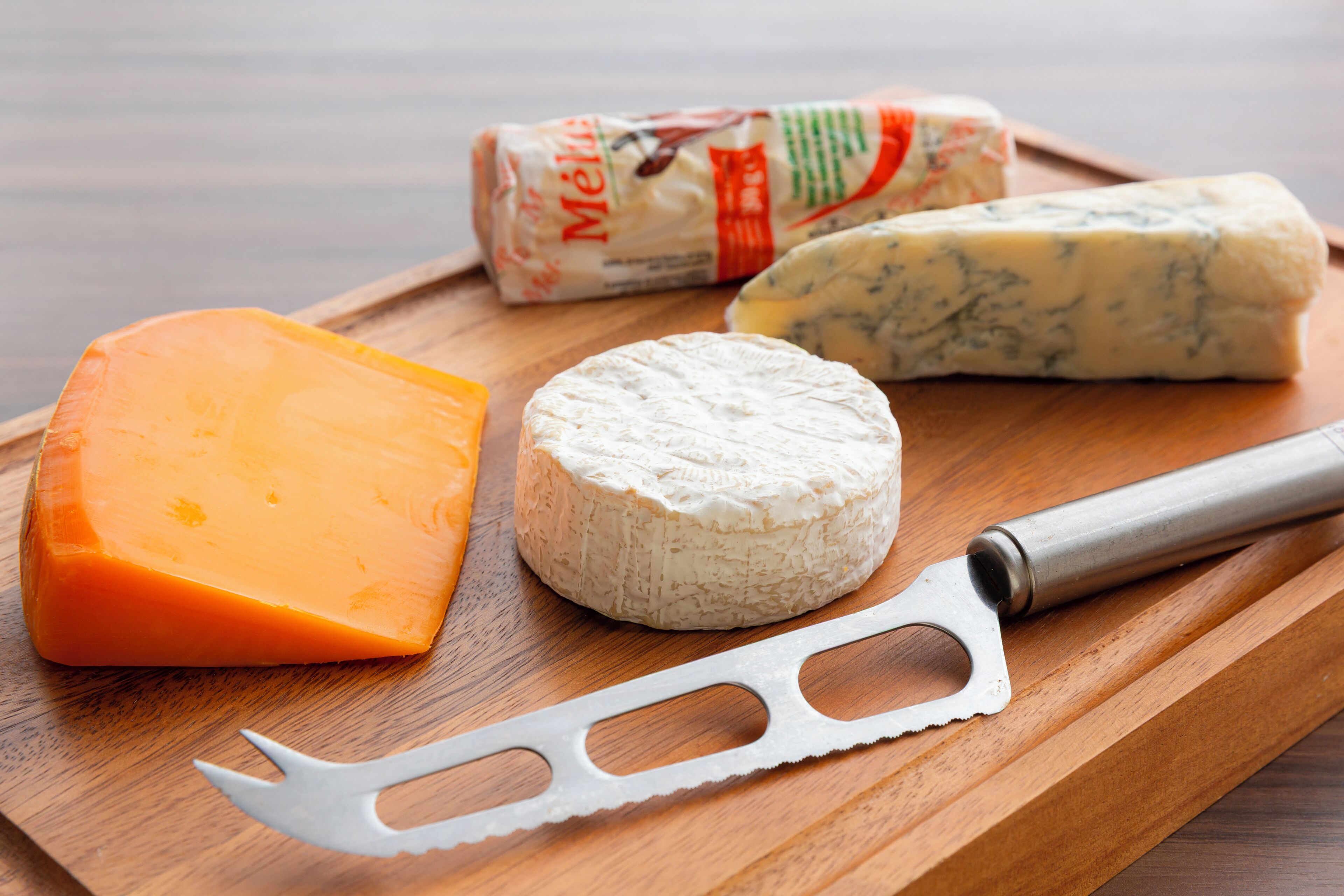 A wooden cutting board with various cheeses and a cheese knife.
