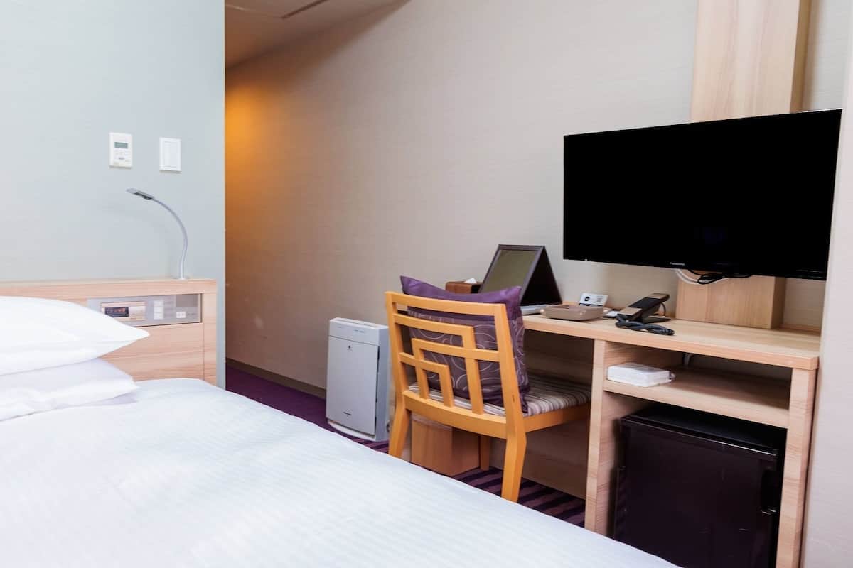A hotel room with a bed, a desk with a computer, a TV, and a small refrigerator.