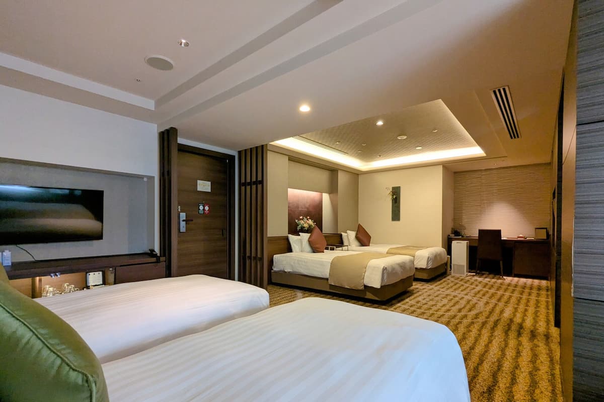 A hotel room with two beds, a desk, a TV, and a mirror.