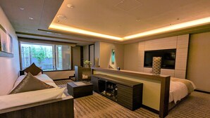 Habitación de hotel moderna con una cama grande, una zona de estar con una mesa de café, una chimenea y un amplio ventanal con vistas al exterior.