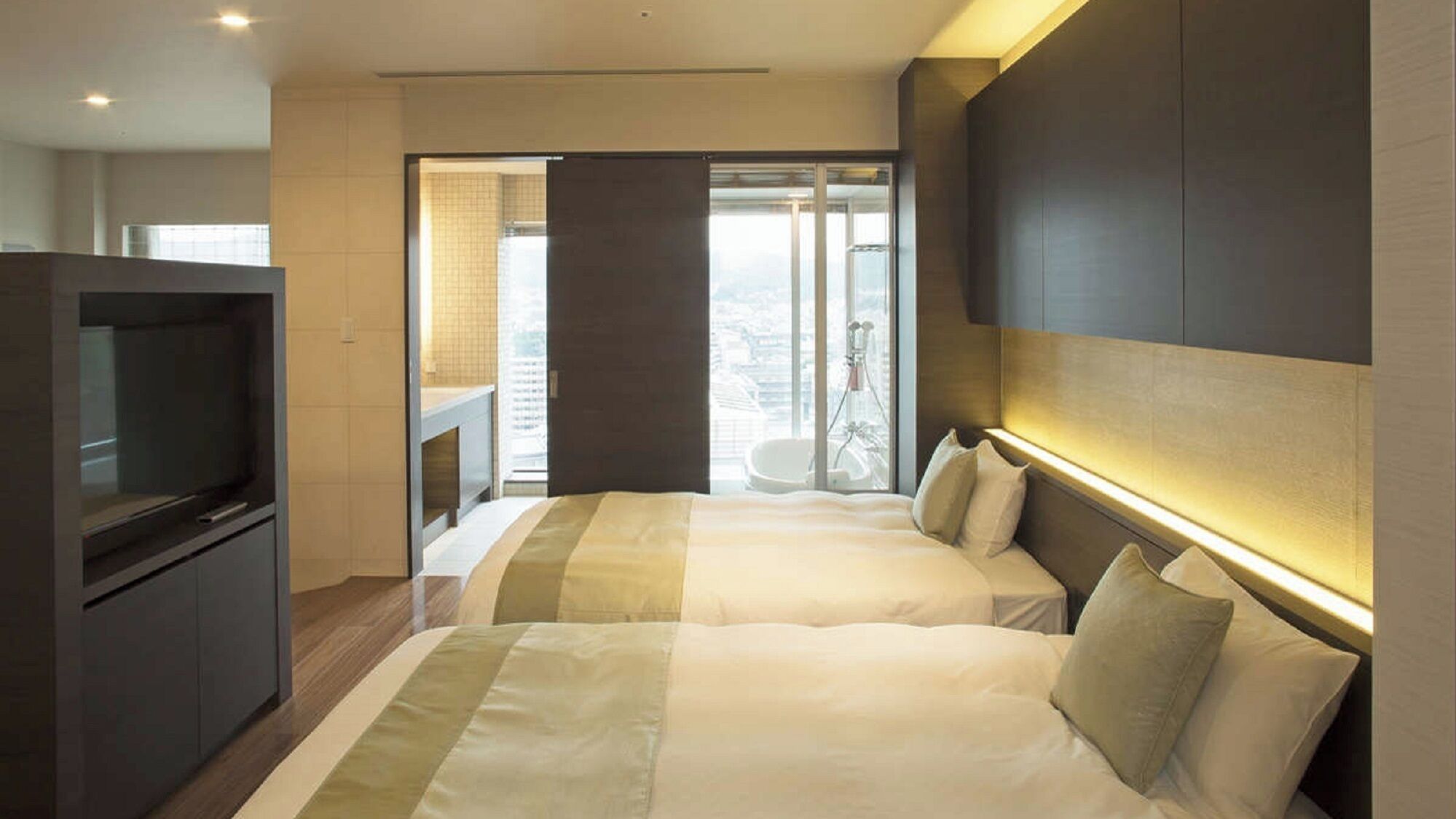 Habitación de hotel con dos camas, televisión y balcón con vista a la ciudad.